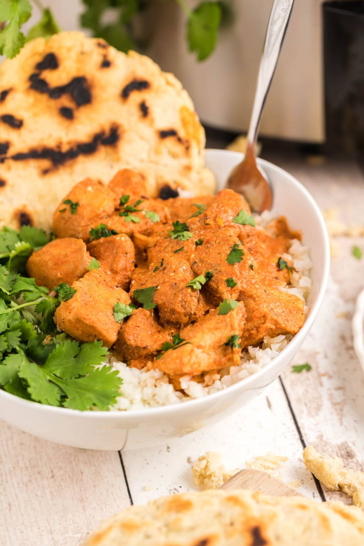 A bowl of chicken curry on rice, garnished with cilantro and served with flatbread—try this easy slow cooker recipe for a flavorful meal that’s simple to make any night of the week.