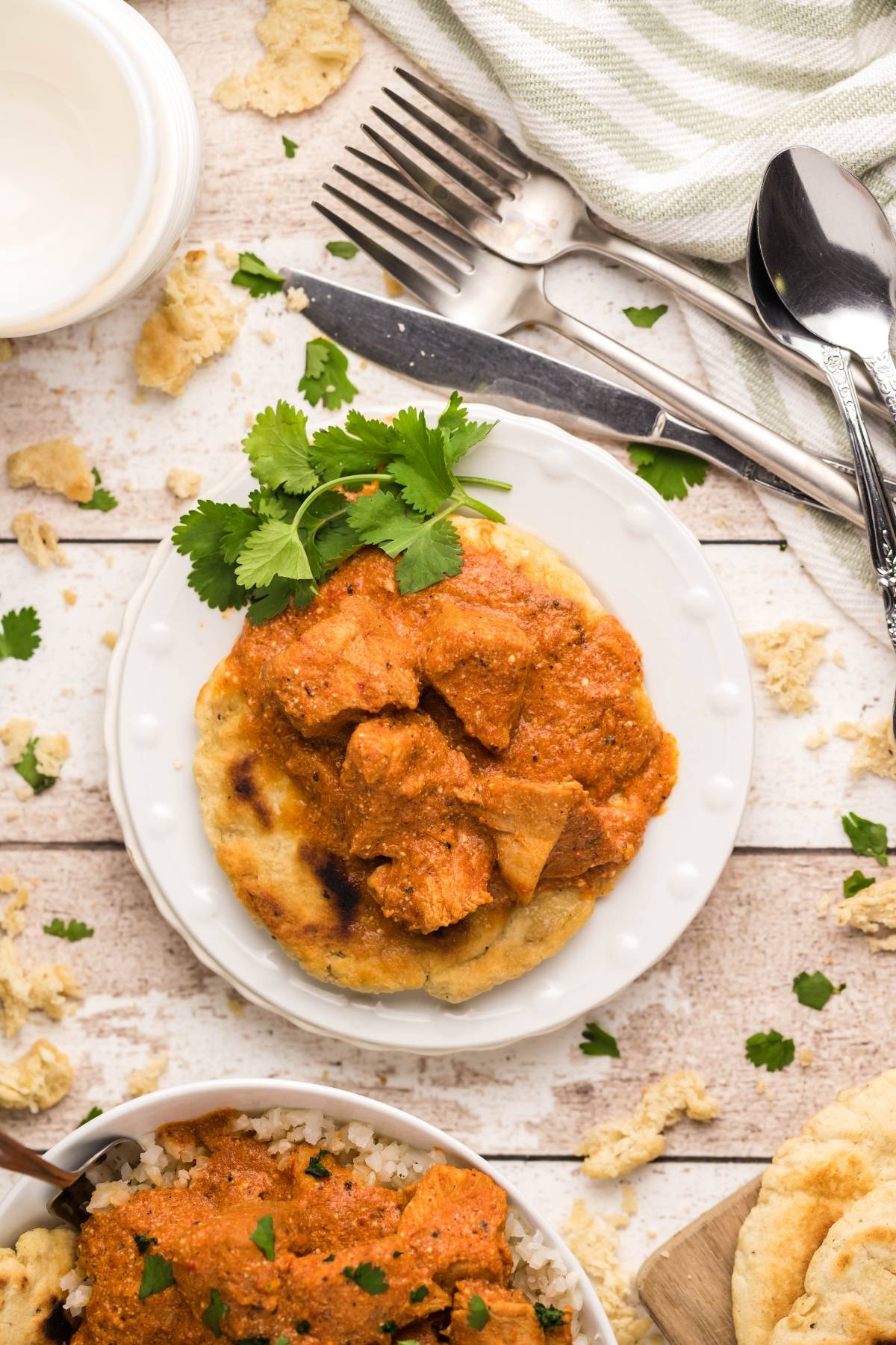 A plate with chicken curry on a flatbread, garnished with cilantro, sits next to cutlery and a striped napkin—a delicious chicken curry recipe perfect for any meal.