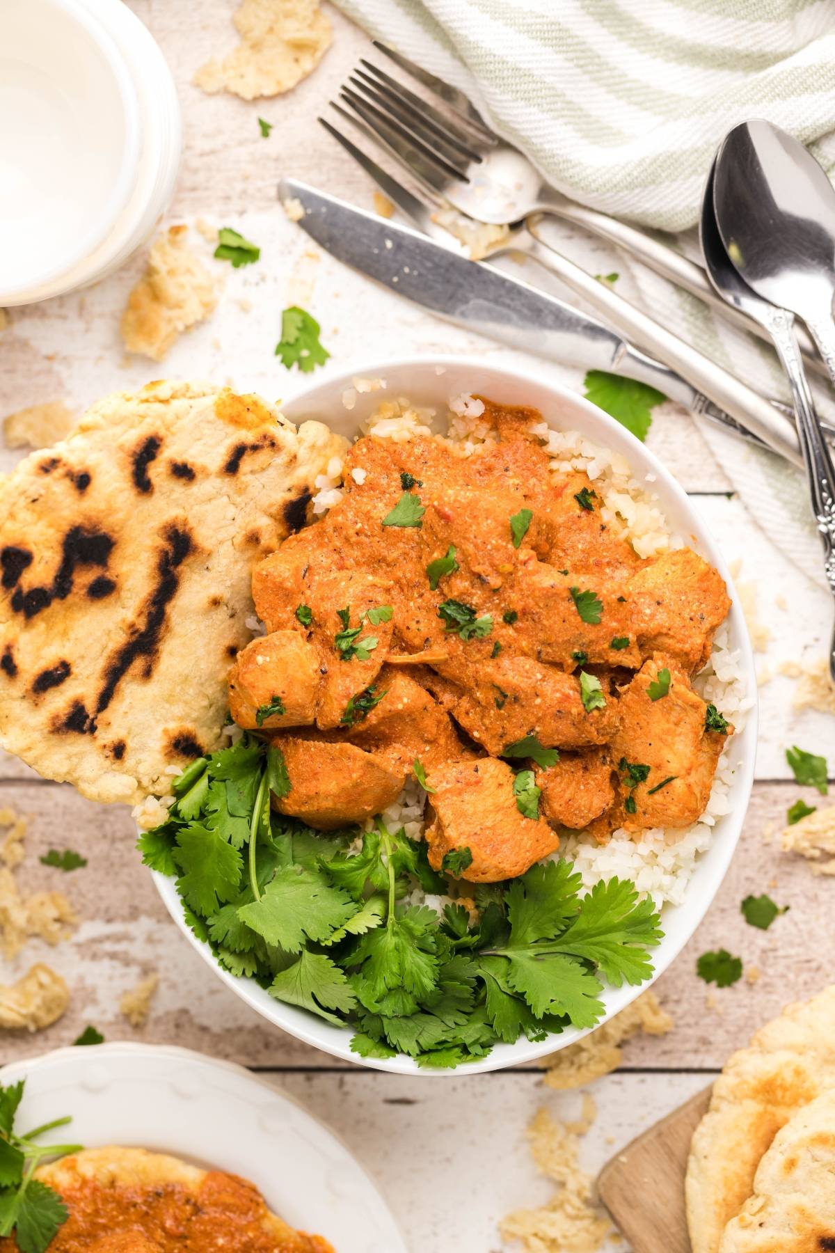 A bowl of chicken curry with rice, naan bread, and fresh cilantro, inspired by a classic chicken curry recipe, with utensils and a napkin nearby.