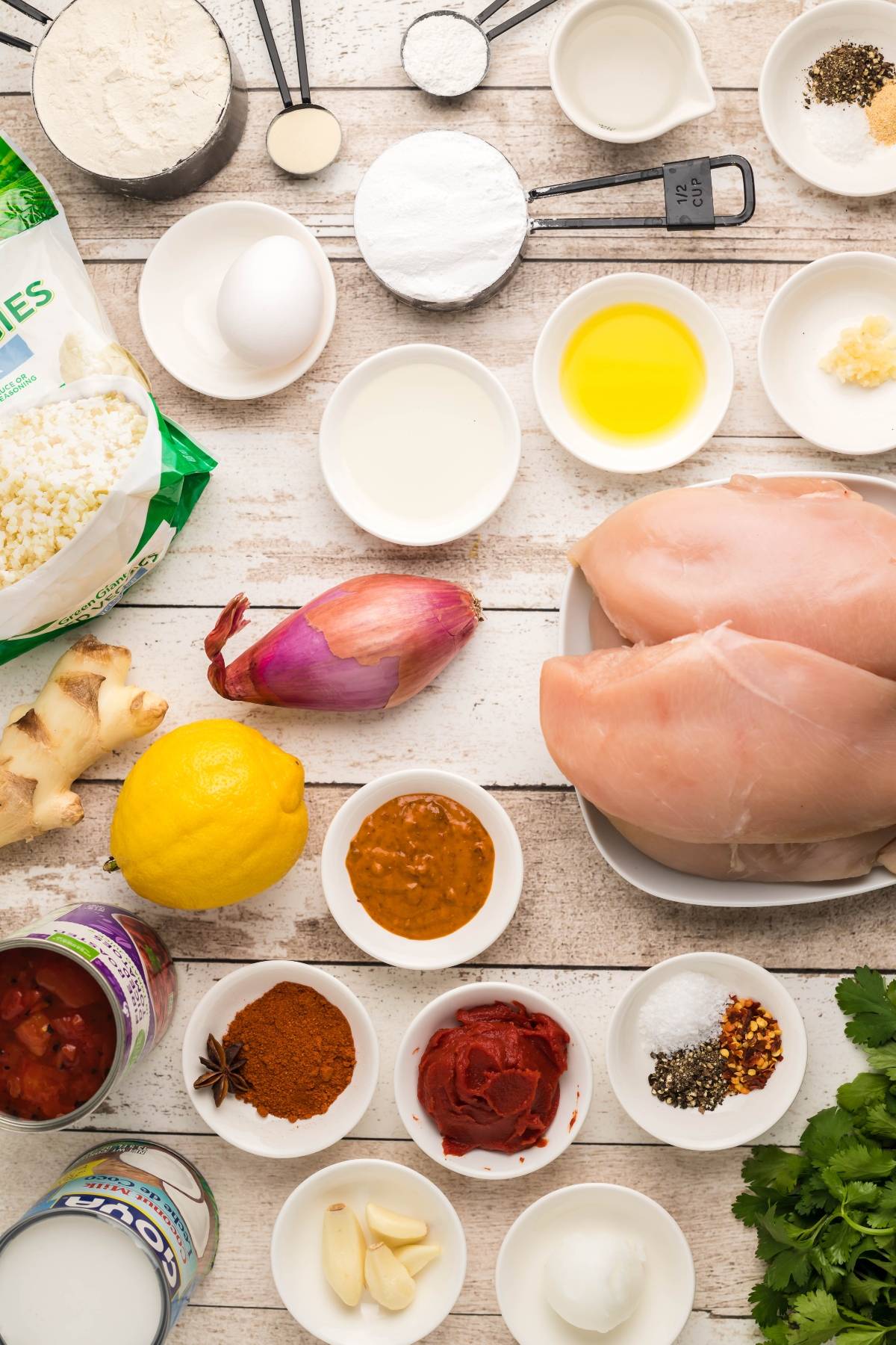 Various fresh ingredients and spices, including chicken breasts, lemon, egg, and herbs, arranged on a white surface—perfect for creating a flavorful slow cooker butter chicken at home.