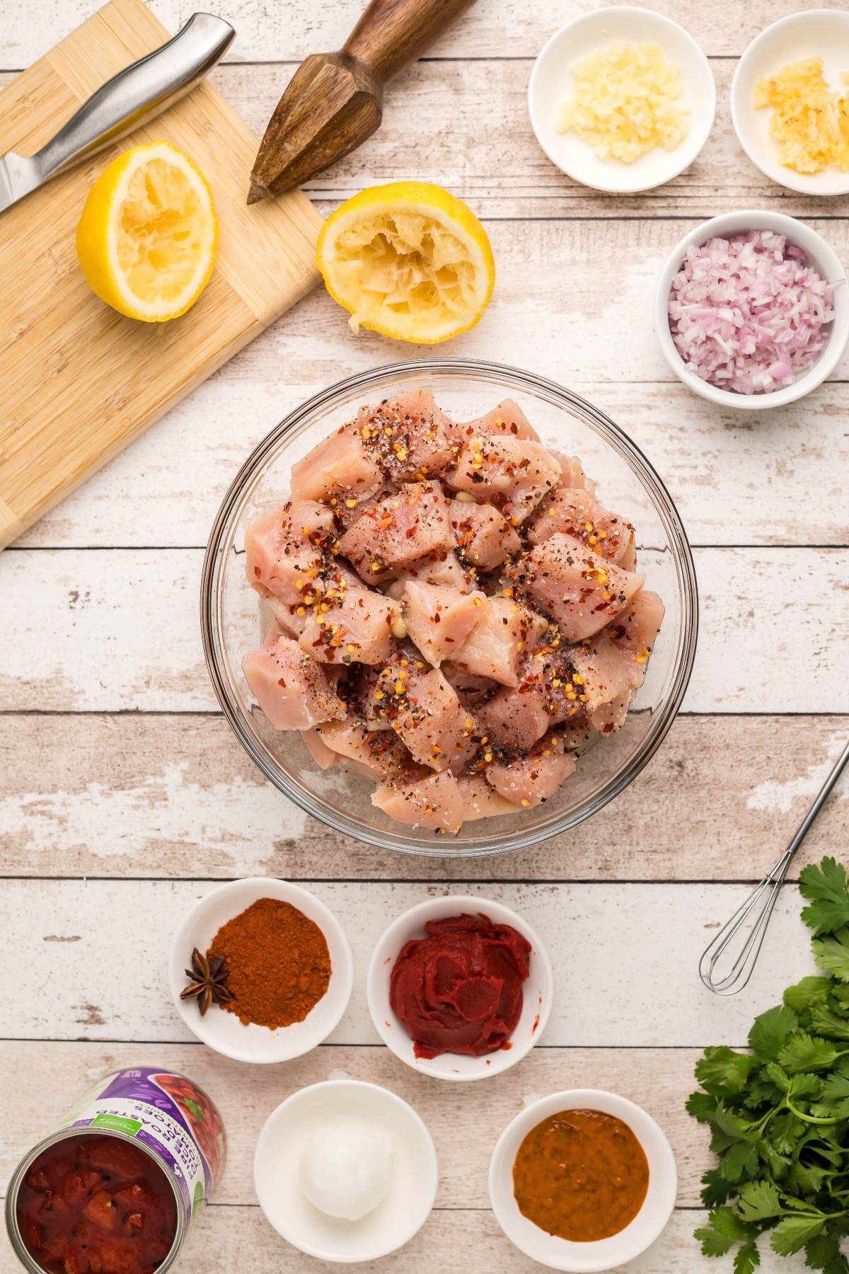 Top view of diced raw chicken in a bowl, surrounded by spices, chopped onion, garlic, lemon, and herbs—perfect for an easy slow cooker butter chicken or your favorite chicken curry recipe.