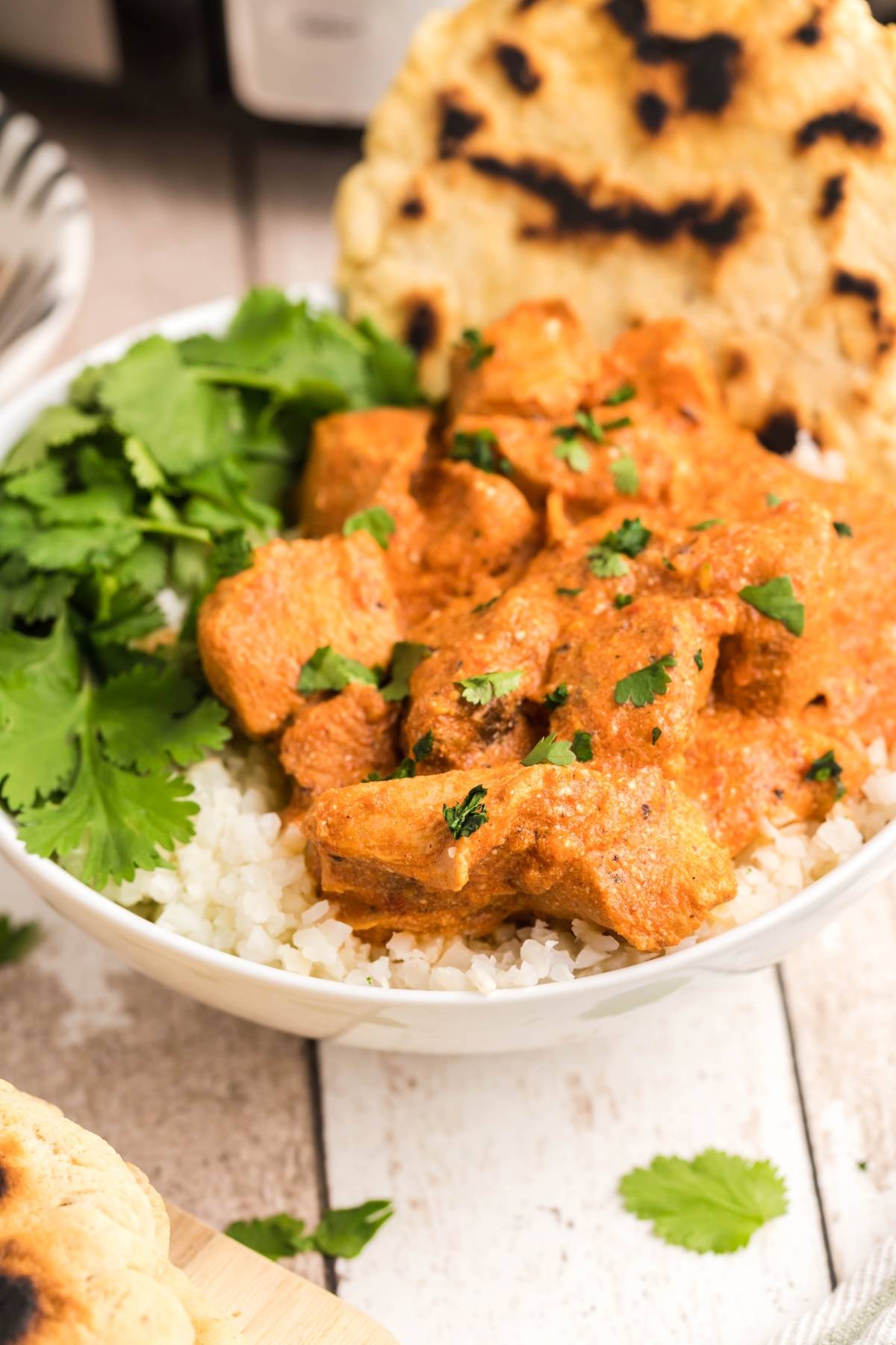 A bowl of slow cooker butter chicken on rice, garnished with cilantro and served with naan bread.