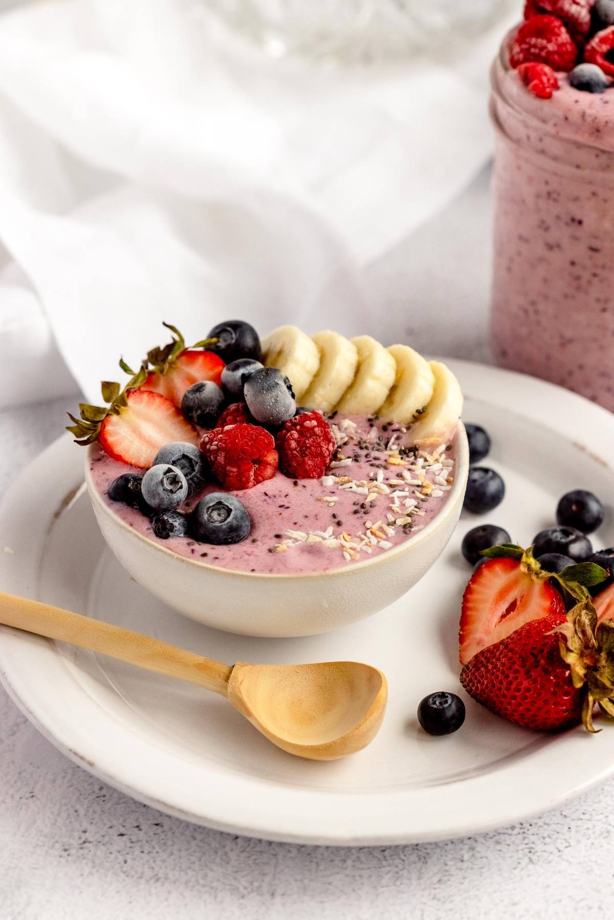 A smoothie bowl topped with banana slices, strawberries, raspberries, blueberries, and seeds on a white plate—perfect for DIY Meal Prep using homemade smoothie packs or frozen smoothie bags.