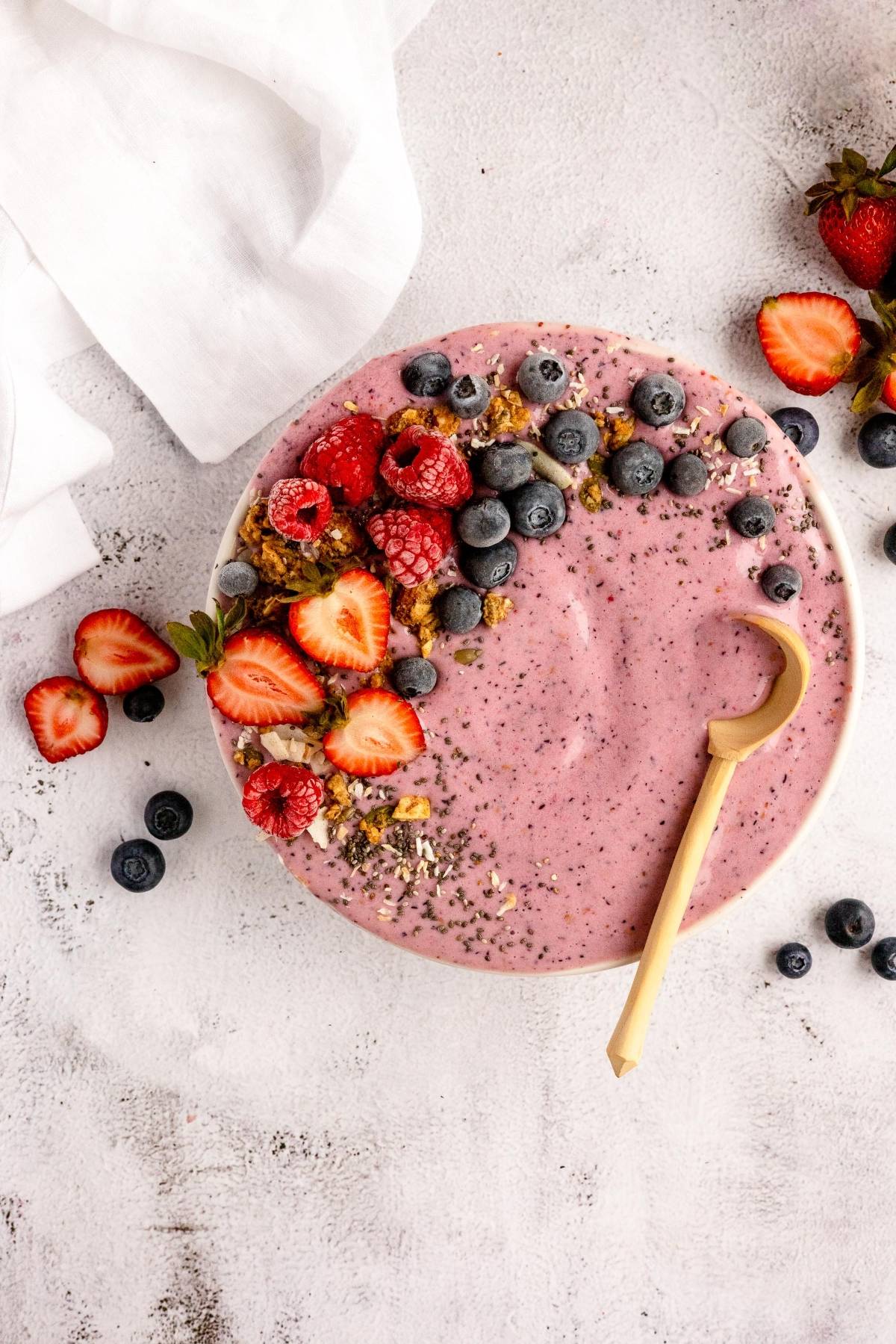 Pink smoothie bowl made with a homemade smoothie pack, topped with granola, strawberries, blueberries, raspberries, chia seeds, and served with a spoon—perfect for easy DIY meal prep!.