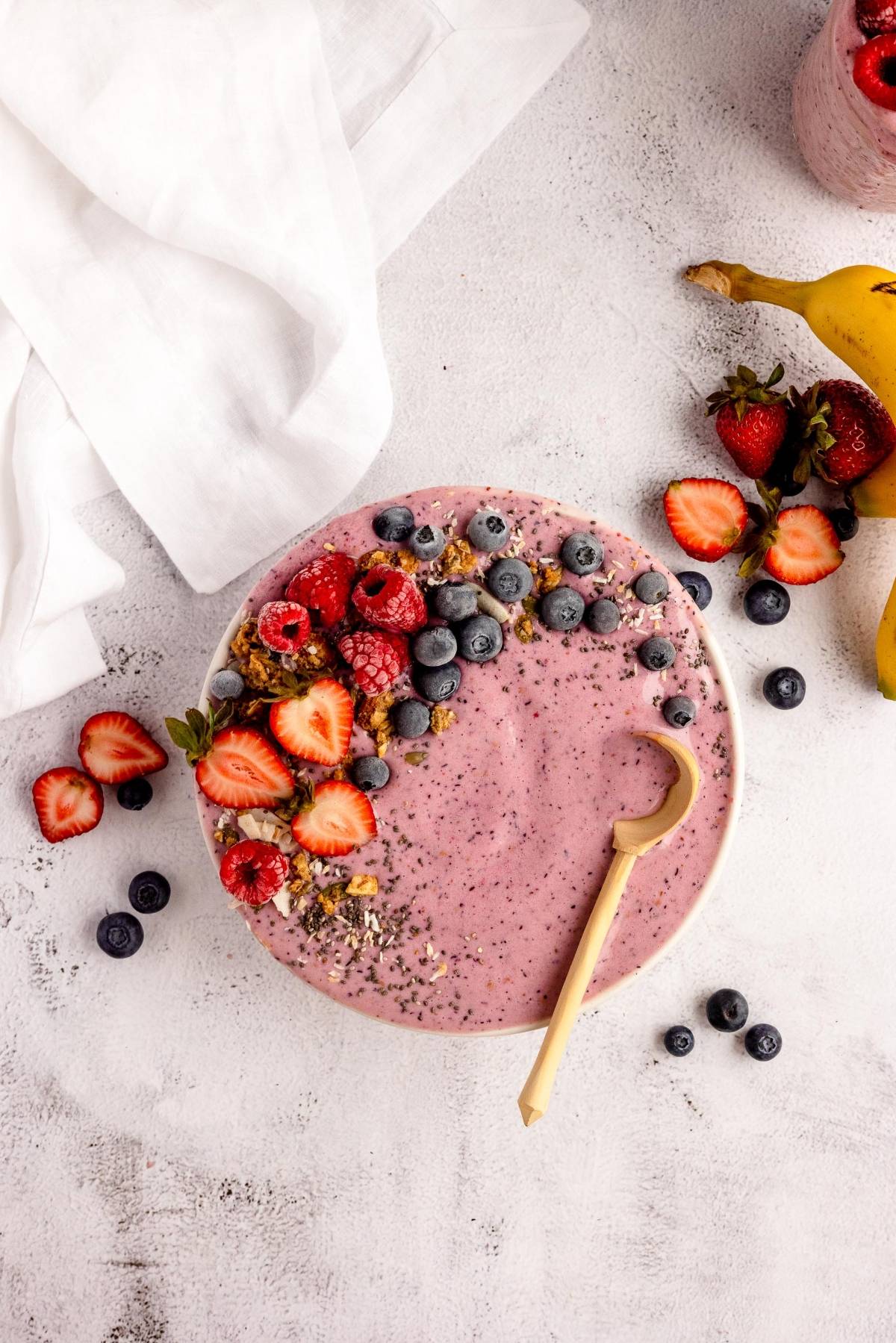 A smoothie bowl topped with strawberries, blueberries, raspberries, granola, and a small wooden spoon—perfect for using your homemade smoothie pack or Smoothie Freezer Packs - DIY Meal Prep.