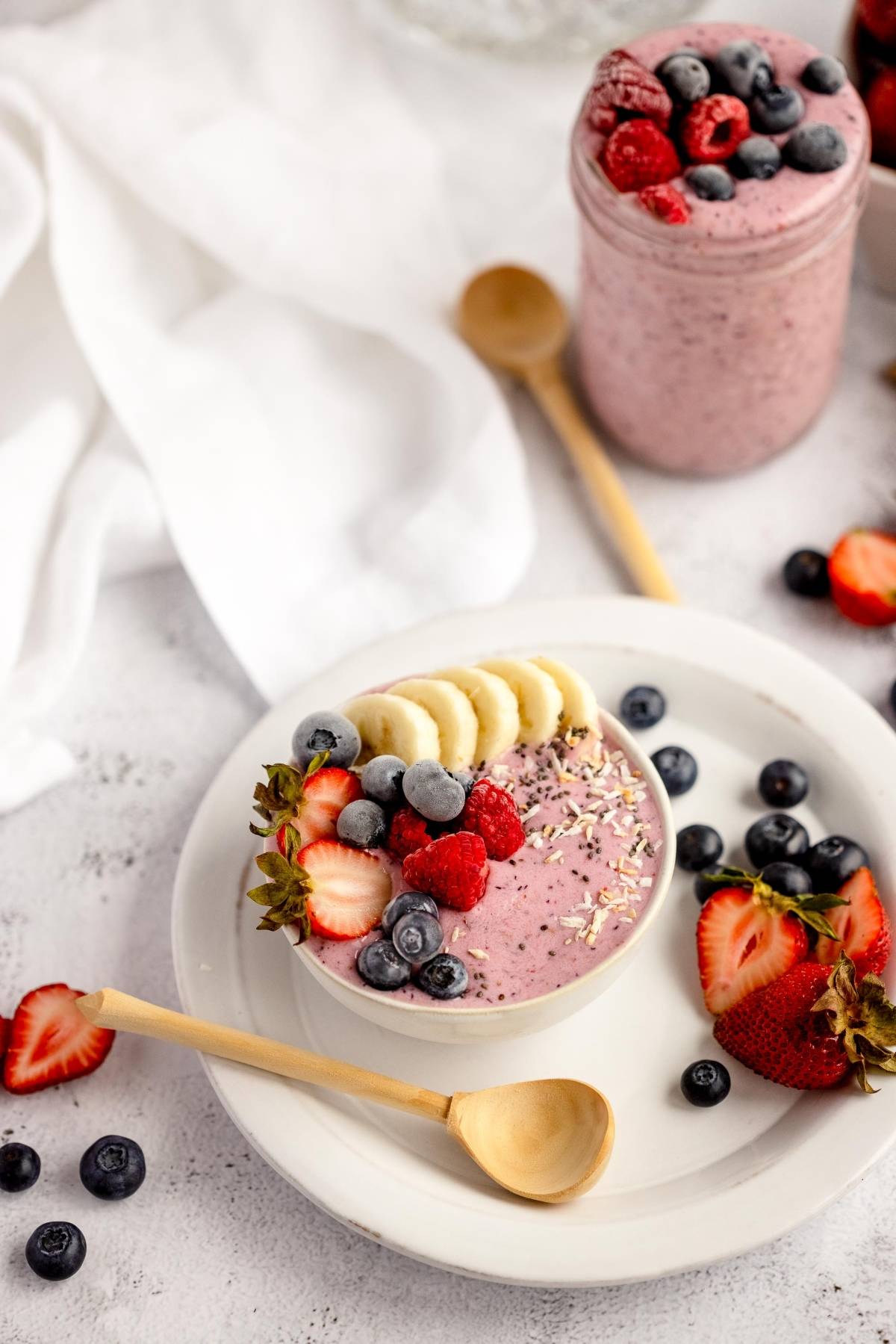 A smoothie bowl topped with banana, berries, and seeds, made easy with frozen smoothie bags—perfect for quick breakfasts. A wooden spoon rests nearby surrounded by scattered fruit.