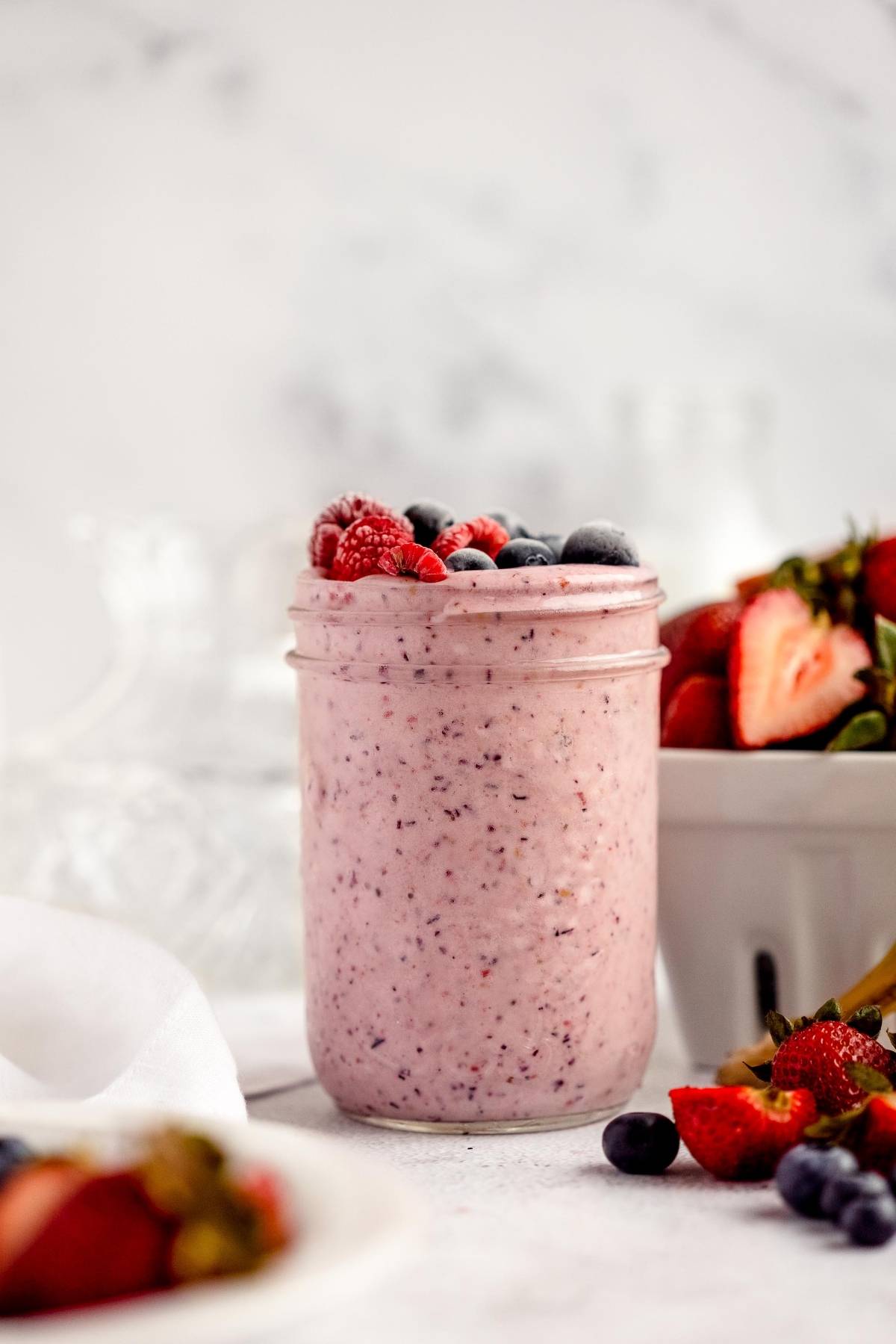 A jar of berry smoothie topped with raspberries and blueberries sits next to a bowl of fresh strawberries—perfect for DIY Meal Prep or as part of your make ahead smoothie mix routine.
