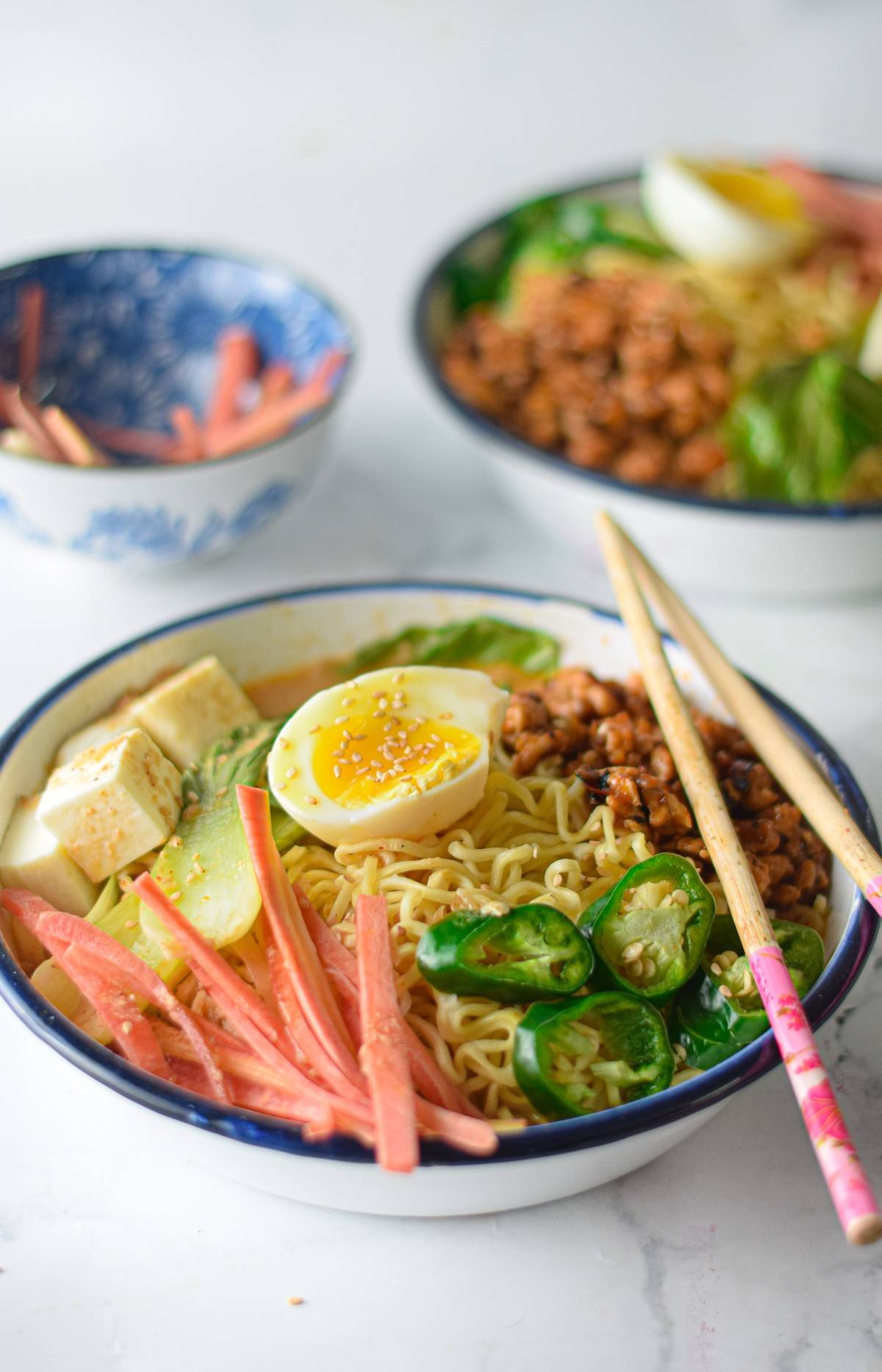 A bowl of ramen recipe topped with egg, tofu, vegetables, and chopsticks resting on the rim.