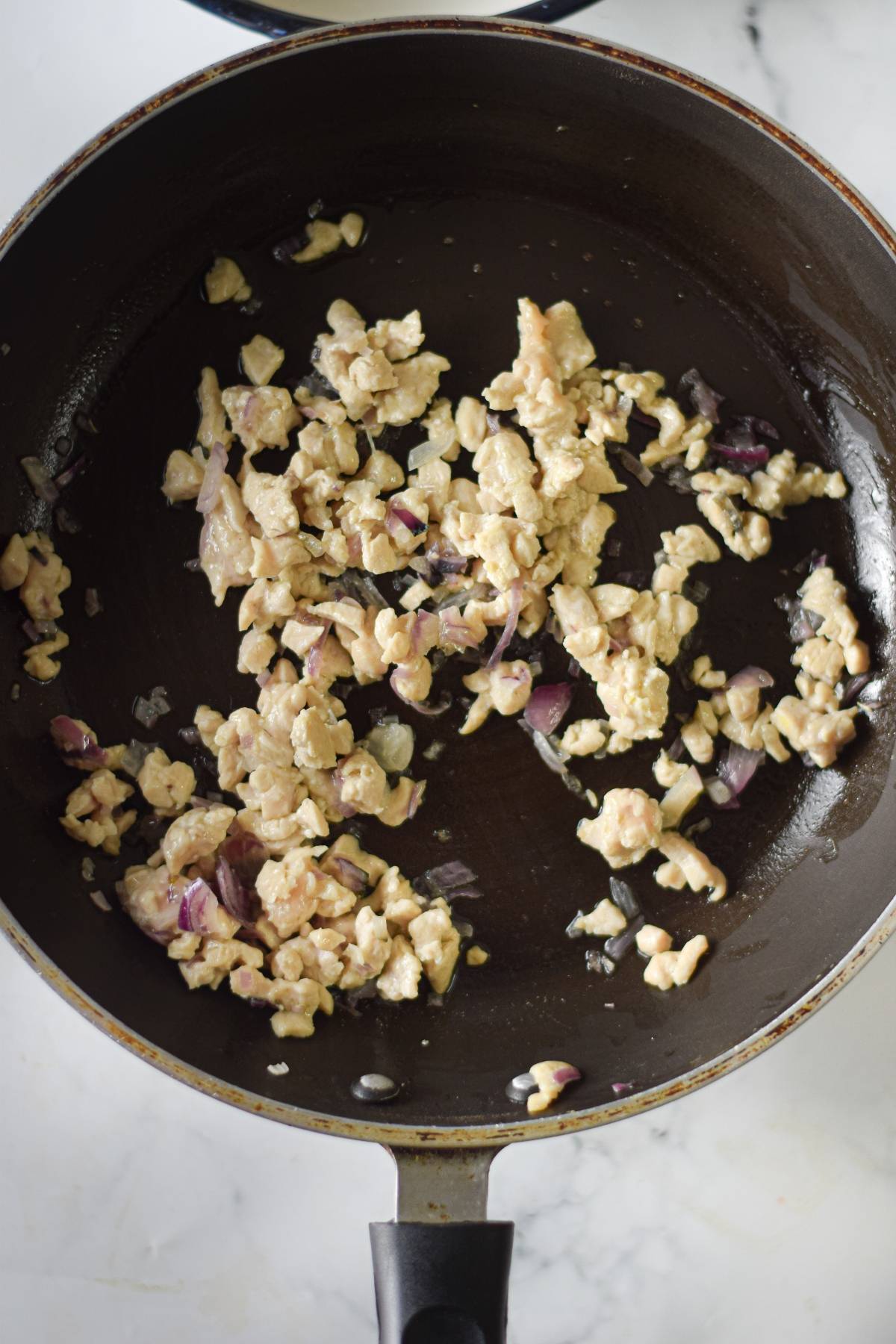 Ground chicken and chopped red onions are sautéed in a nonstick frying pan on the stovetop, creating a flavorful base for your next Spicy Chicken Miso Ramen.