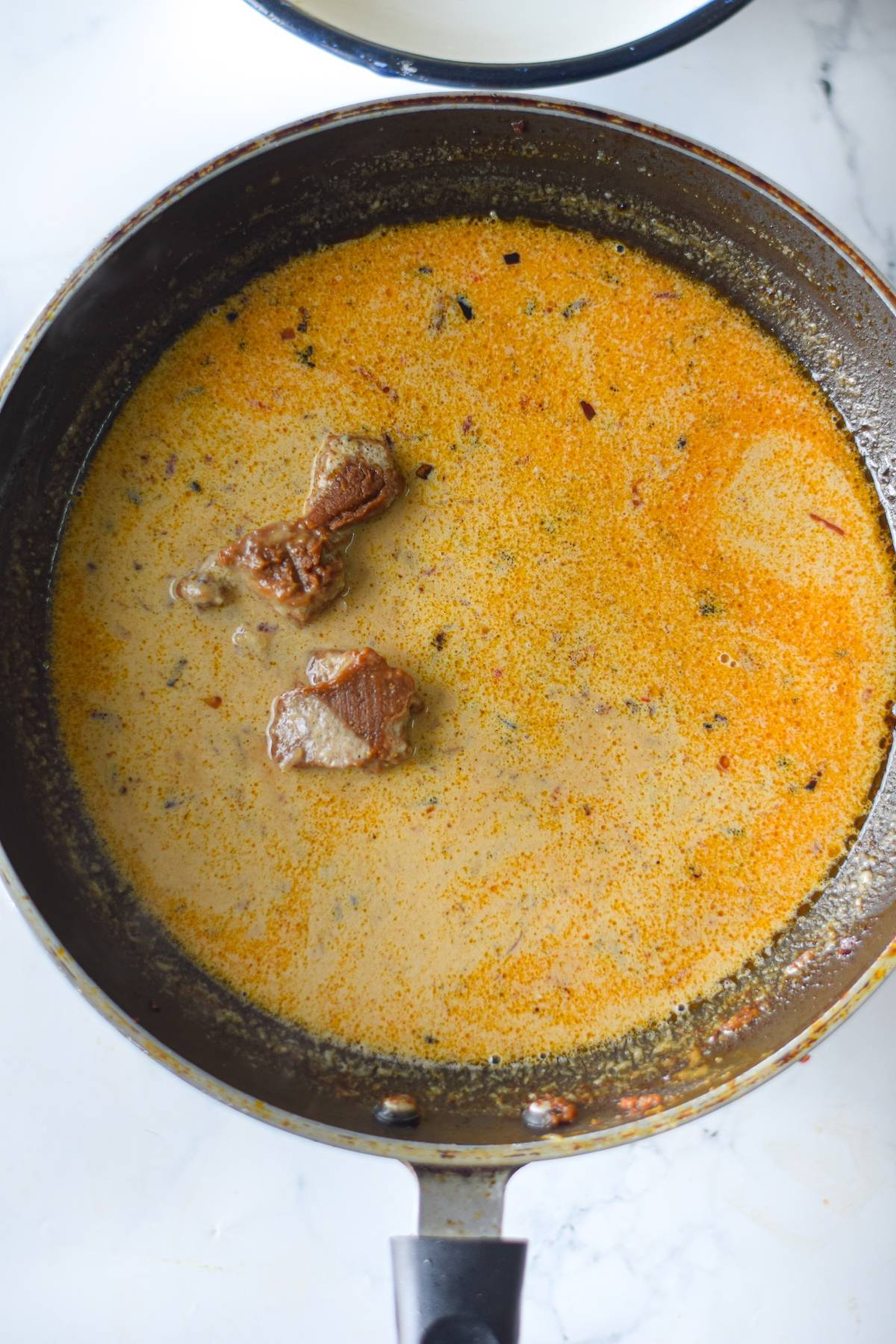 A skillet filled with creamy orange curry sauce and tender pieces of cooked meat, reminiscent of a spicy tahini recipe.