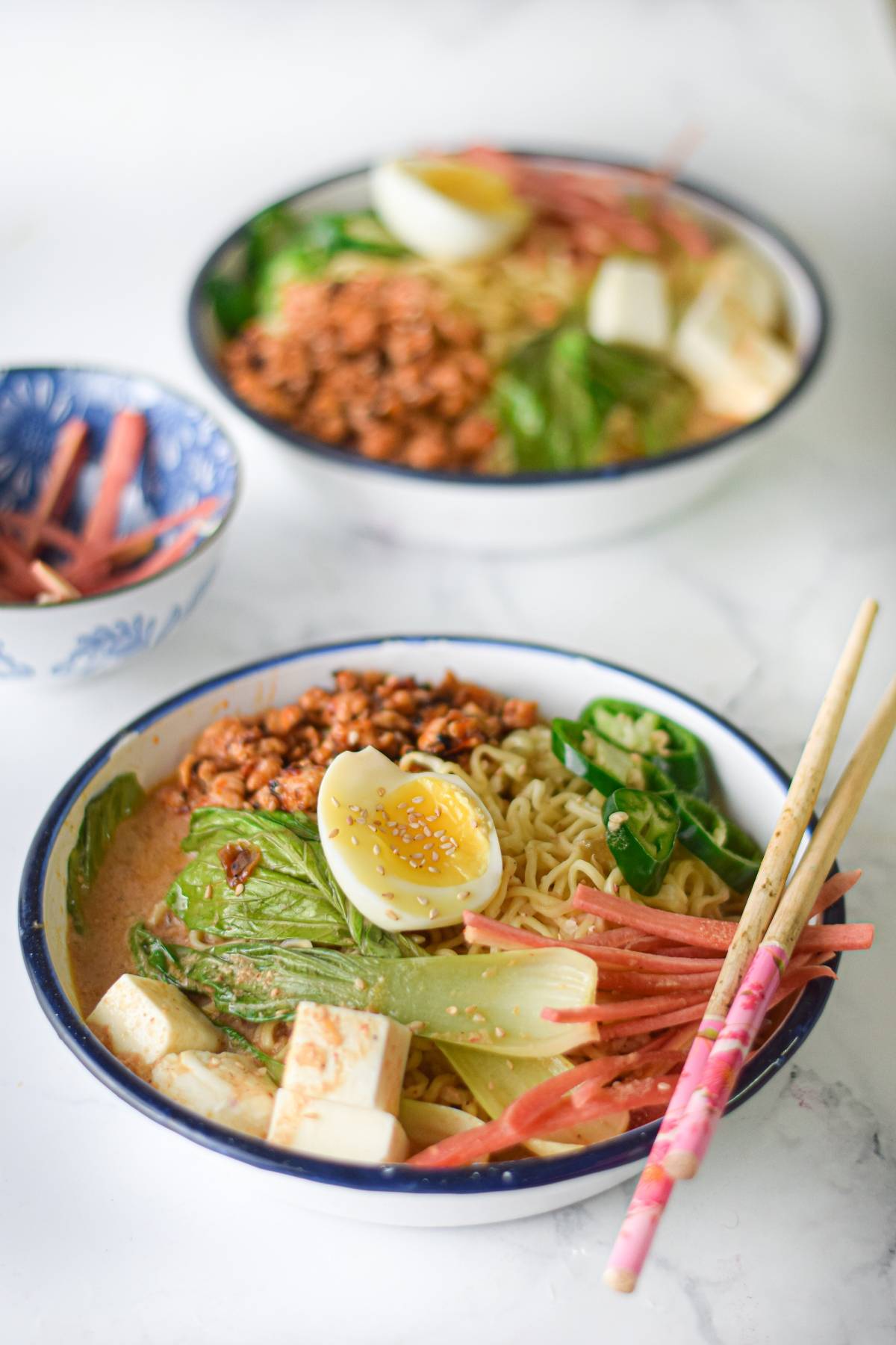 Bowl of Spicy Chicken Miso Ramen with boiled egg, tofu, greens, sliced meat, and chopsticks on the side.