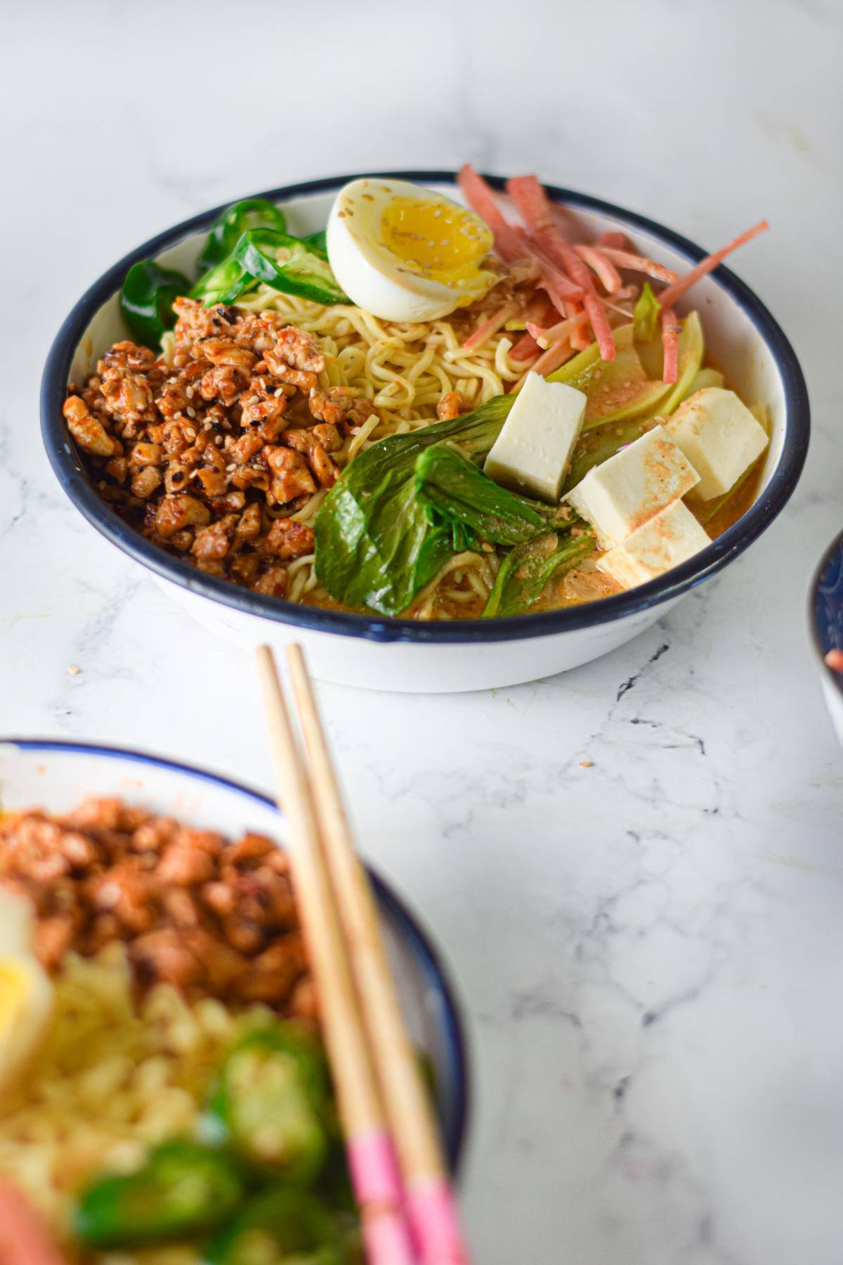 A bowl of ramen with chicken and tofu, minced meat, greens, half a boiled egg, and pickled vegetables—a flavorful ramen recipe for comfort and warmth.
