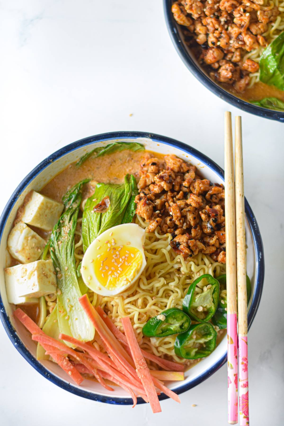 A bowl of ramen with egg, tofu, ground meat, greens, jalapeños, carrots, and chopsticks on the side—perfect for anyone seeking a flavorful ramen recipe packed with fresh ingredients and vibrant colors.