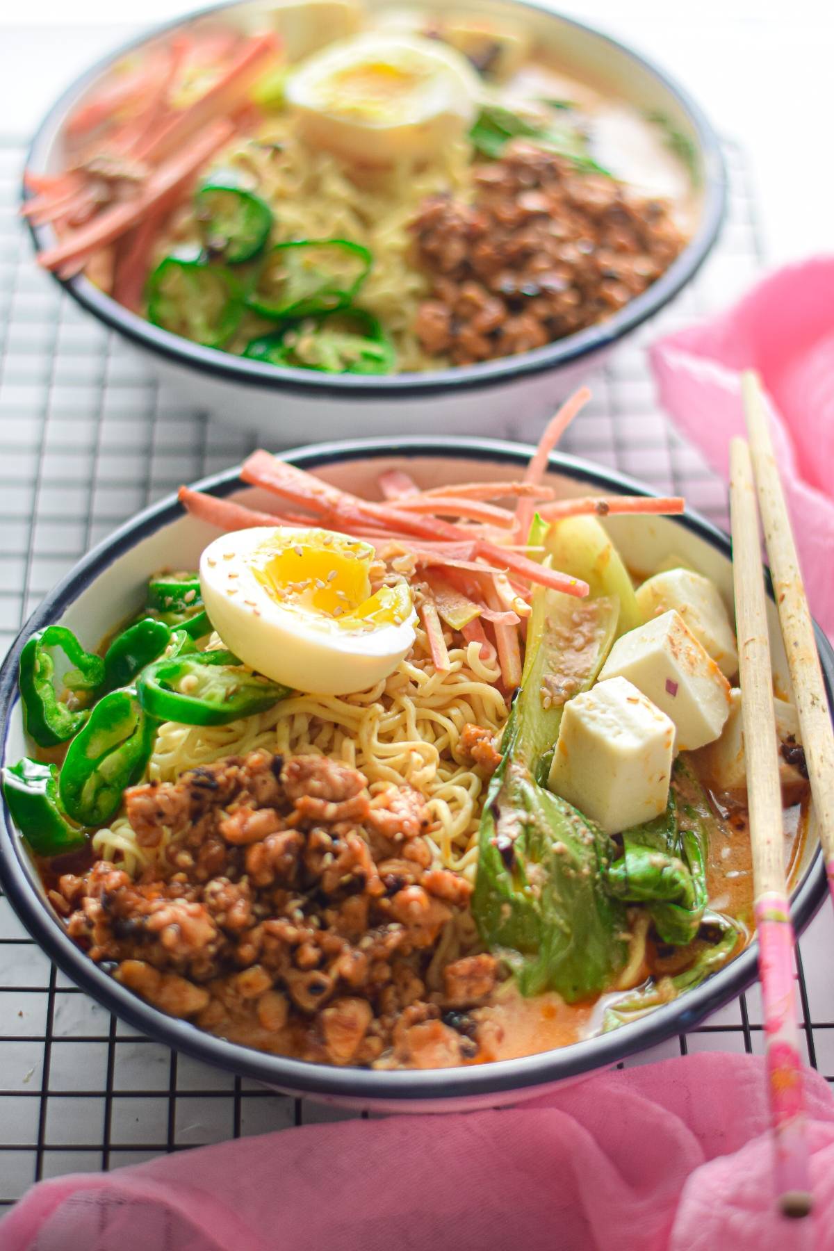 Two bowls of ramen with egg, tofu, vegetables, sliced meat, and ground meat are served with chopsticks on the side—a perfect ramen recipe for those who love hearty flavors.