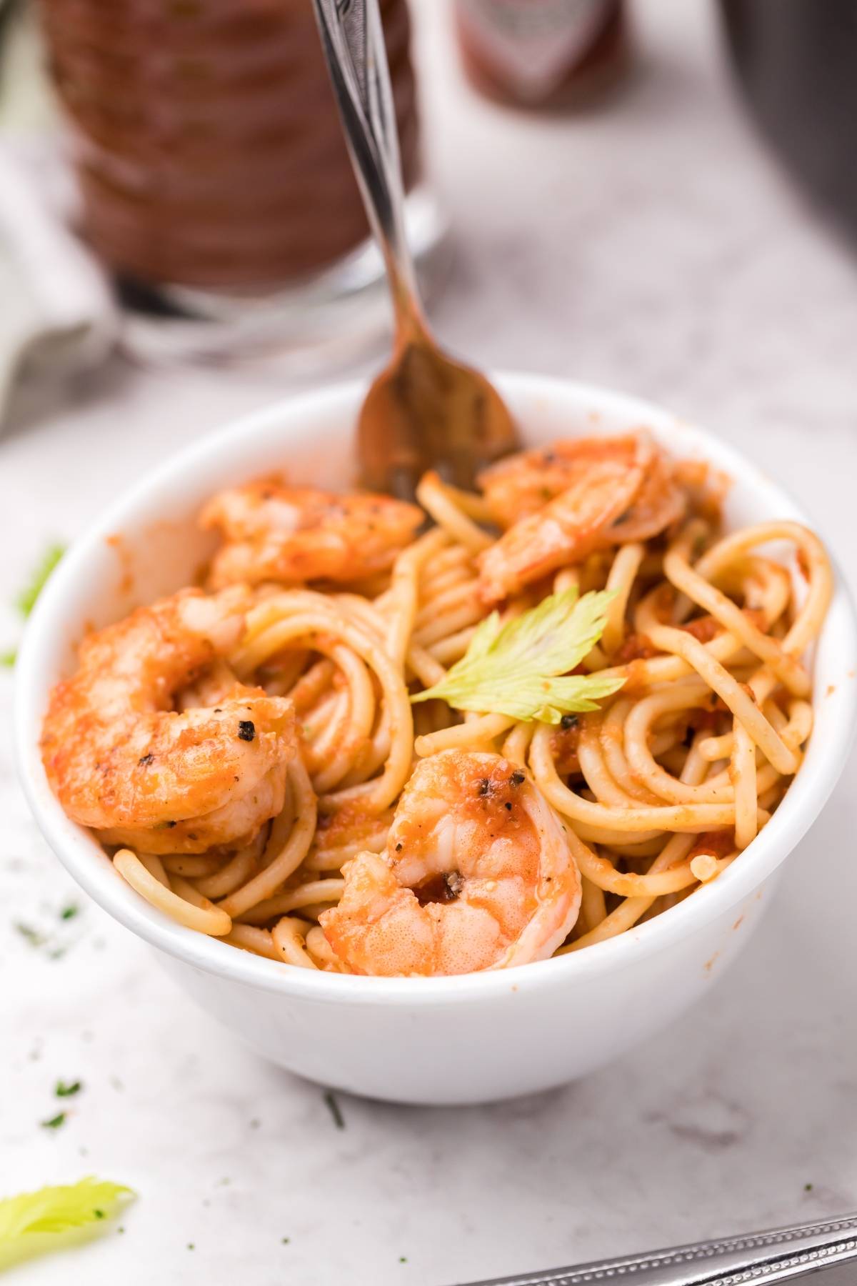 Bowl of spicy shrimp pasta in a rich red Bloody Mary vodka sauce, garnished with celery and served with a fork inside the bowl.
