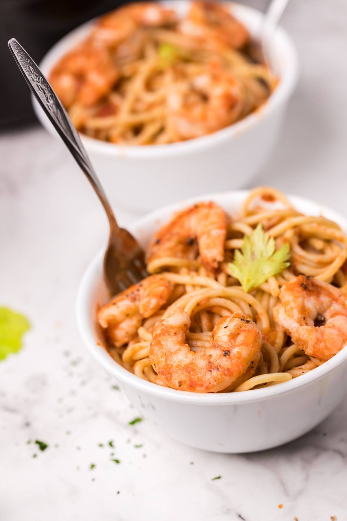 Bowl of spicy shrimp pasta with a fork, featuring a rich Bloody Mary vodka sauce, with another bowl of the same delicious dish in the background.
