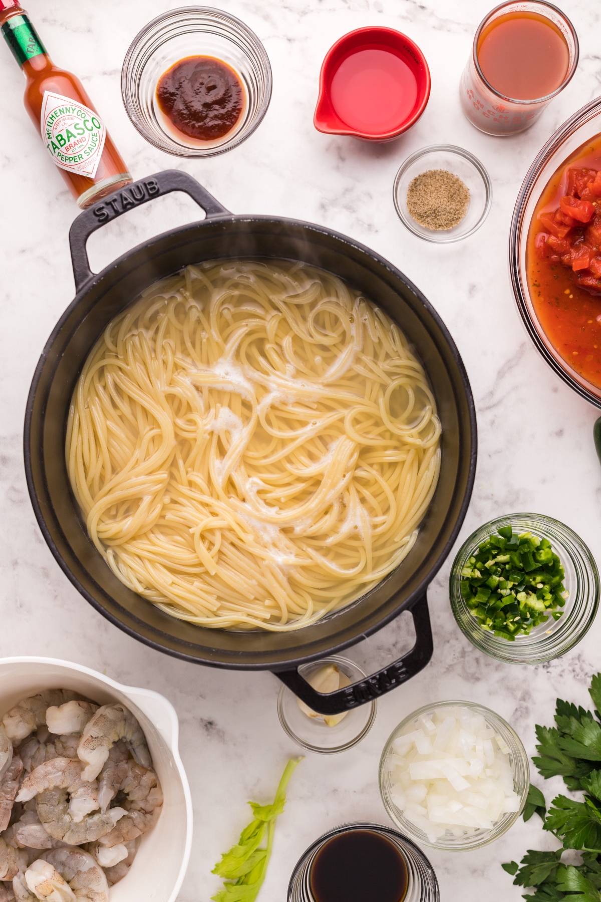 Top-down view of cooked spaghetti in a pot, surrounded by bowls of shrimp, veggies, seasonings, and zesty Bloody Mary vodka sauce—perfect for creating spicy shrimp pasta or classic shrimp pasta with Bloody Mary vodka.