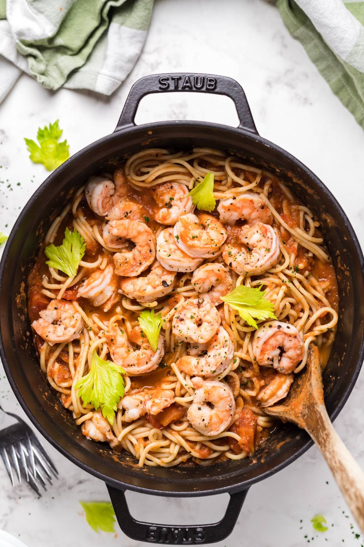 A pot of shrimp pasta with Bloody Mary vodka sauce, featuring tomato sauce and celery leaves, with a wooden spoon resting inside.