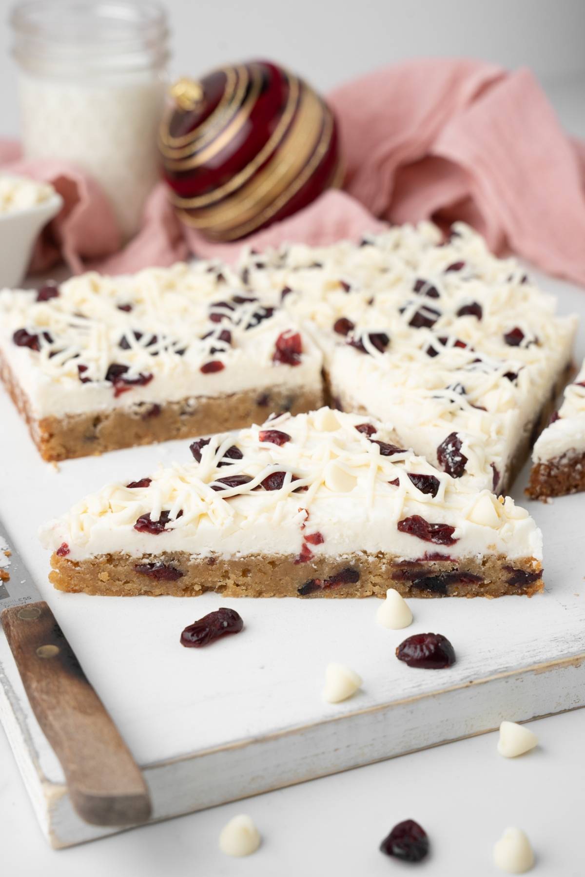 Triangle dessert bars topped with white frosting, dried cranberries, and white chocolate shavings—these homemade bliss bars are a delicious white chocolate cranberry bars copycat recipe you’ll love sharing.