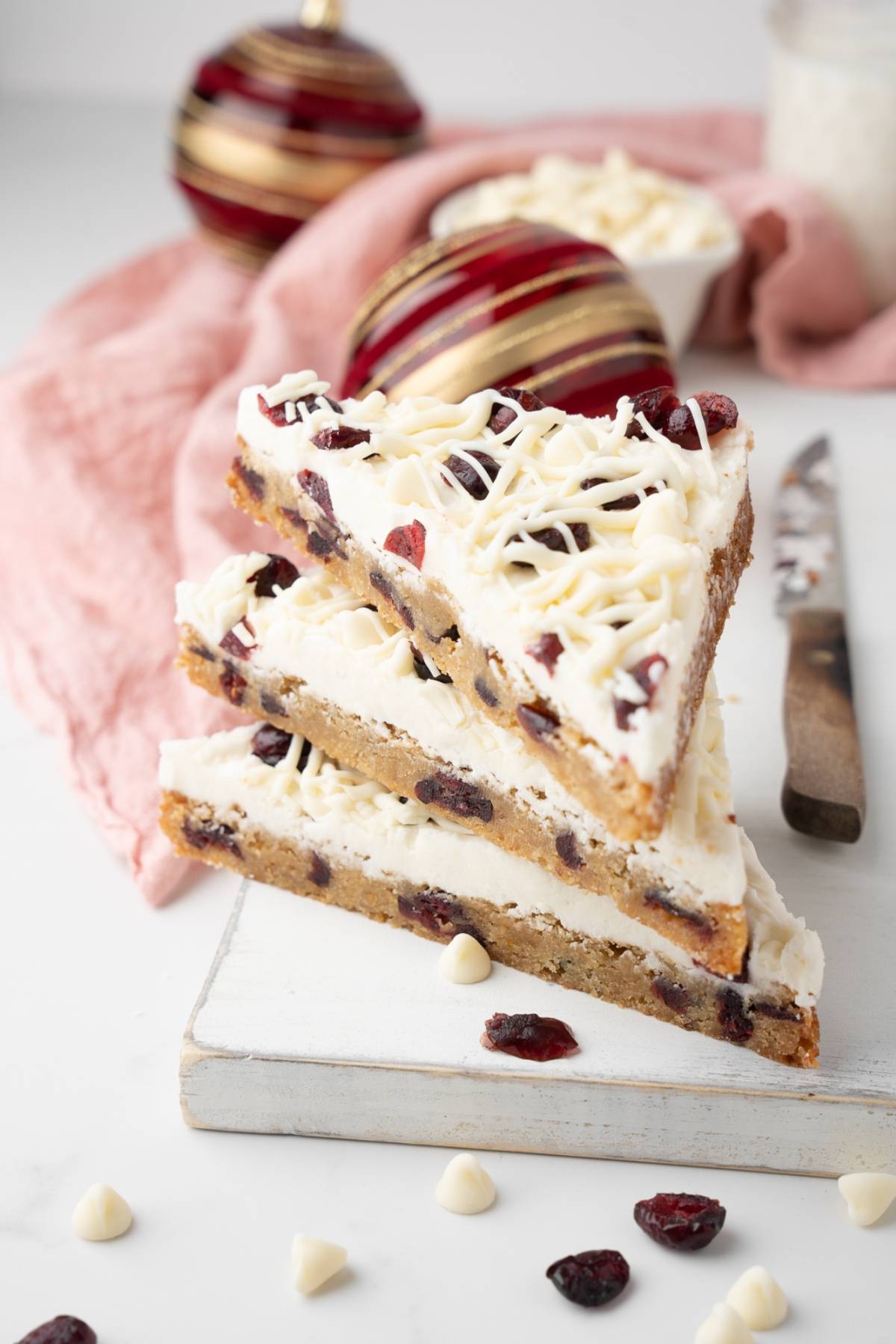 Three triangular white chocolate cranberry bars stacked on a white board, with festive decor behind—just like your favorite Starbucks copycat cranberry bliss bars.