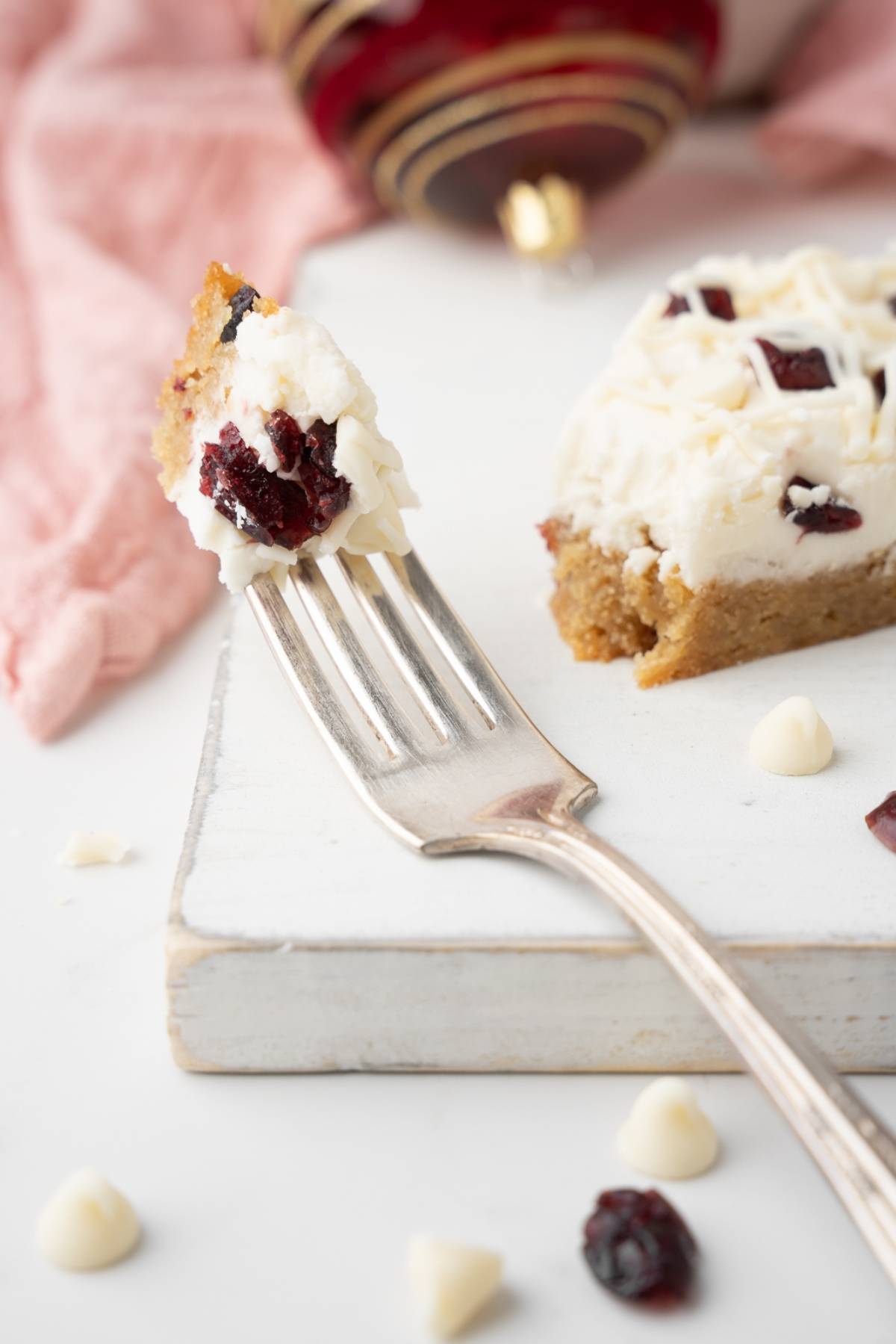 A fork holds a bite of easy cranberry bar with frosting, next to the remaining white chocolate cranberry bar on a white board—just like your favorite copycat recipe.