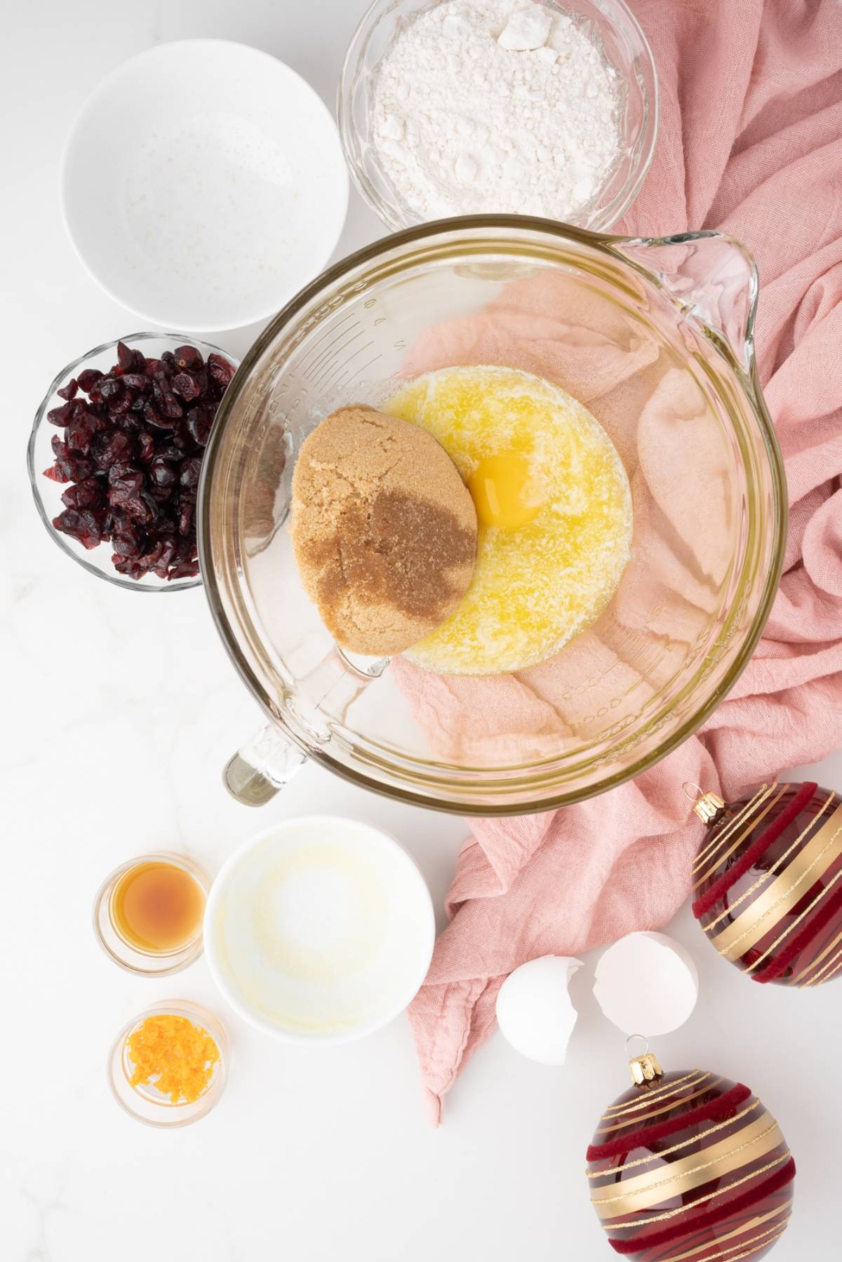 Baking ingredients in bowls on a white counter with a pink cloth and red Christmas ornaments—perfect for making Starbucks copycat cranberry bliss bars.