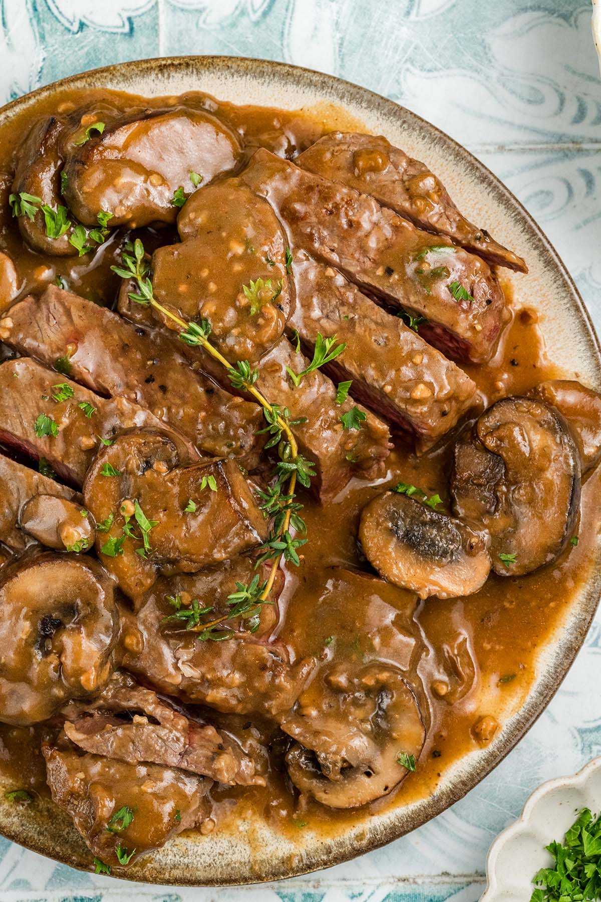 Sliced beef steak marsala with brown mushroom gravy, garnished with fresh herbs on a plate.