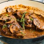 Juicy beef steaks in creamy mushroom sauce, infused with rich Marsala wine and garnished with thyme, sizzle in a large cast iron pan for a classic steak marsala experience.