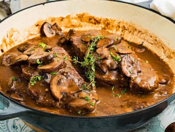 Juicy beef steaks in creamy mushroom sauce, infused with rich Marsala wine and garnished with thyme, sizzle in a large cast iron pan for a classic steak marsala experience.