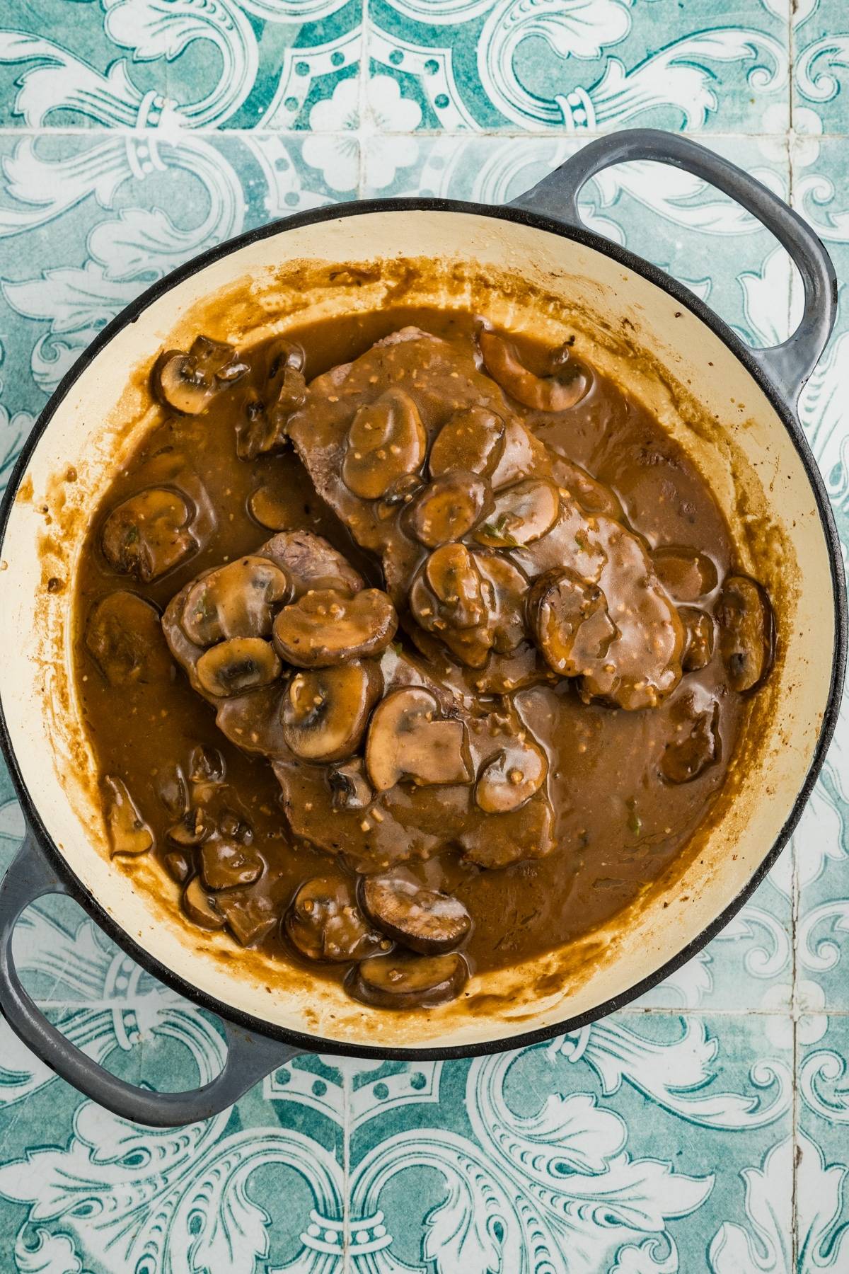 A pot of beef smothered in brown mushroom gravy on a blue and white patterned surface.
