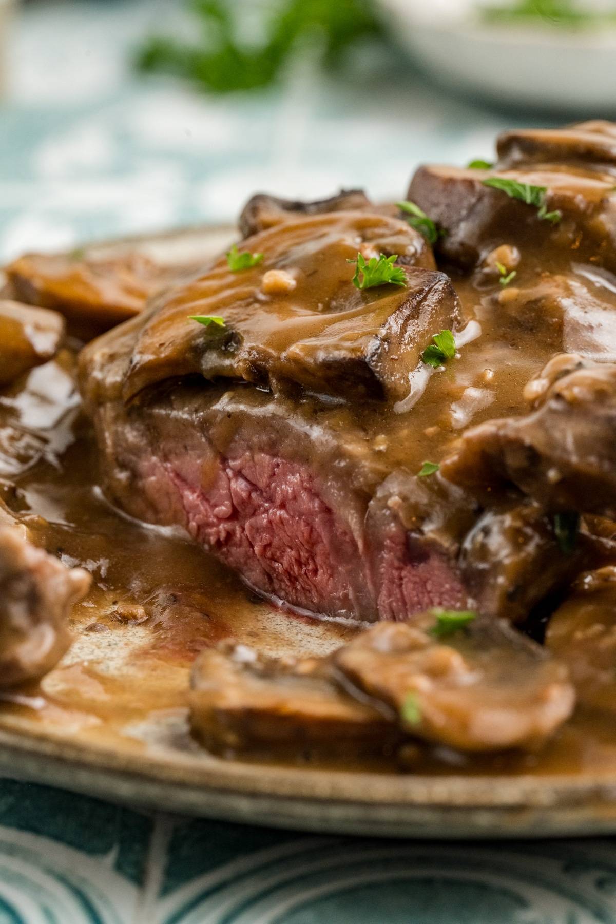 A sliced steak with a pink center, topped with mushroom gravy and garnished with parsley.