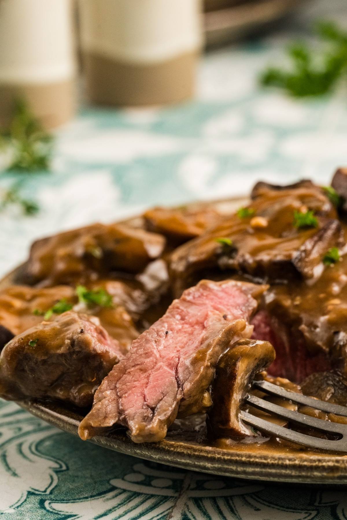 A sliced steak with brown gravy on a plate, garnished with herbs, with a fork holding a piece.