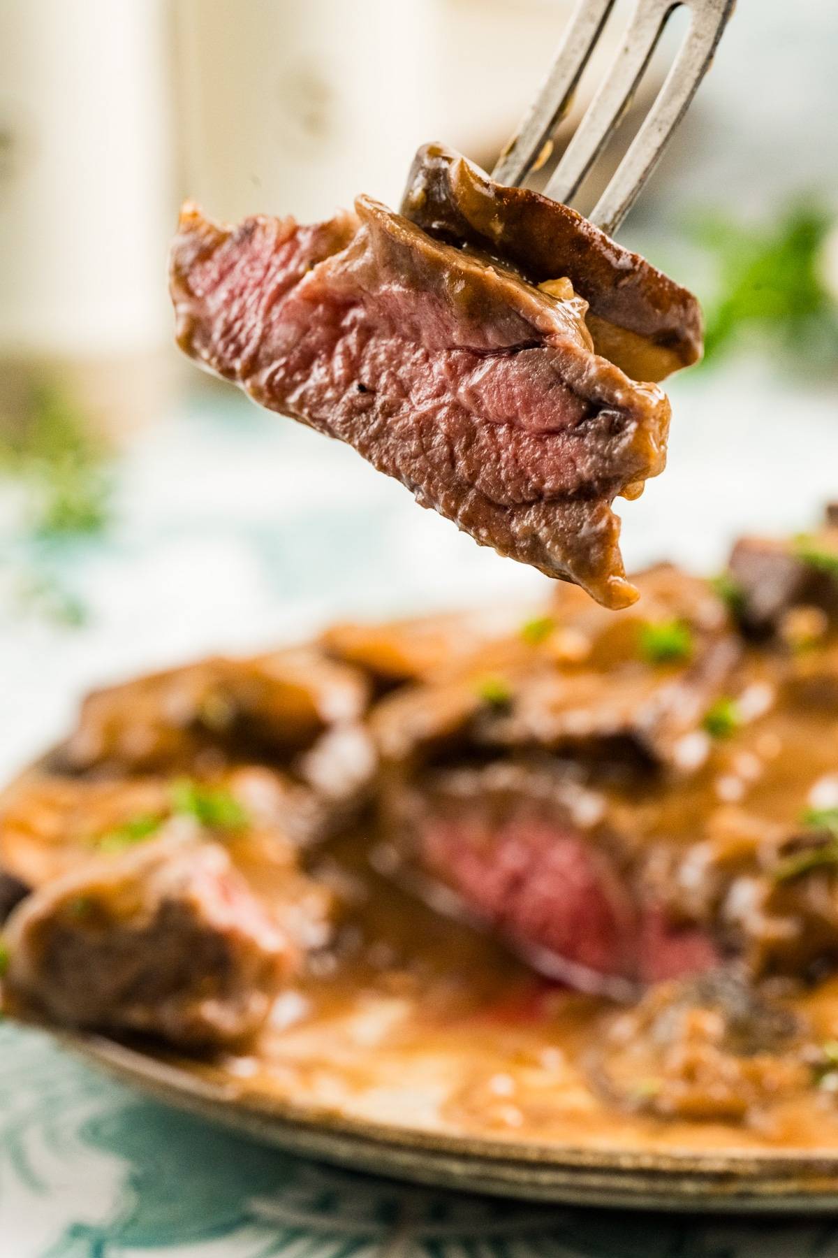 A fork holds a juicy, medium-rare steak slice above a plate with marsala sauce and more steak pieces.