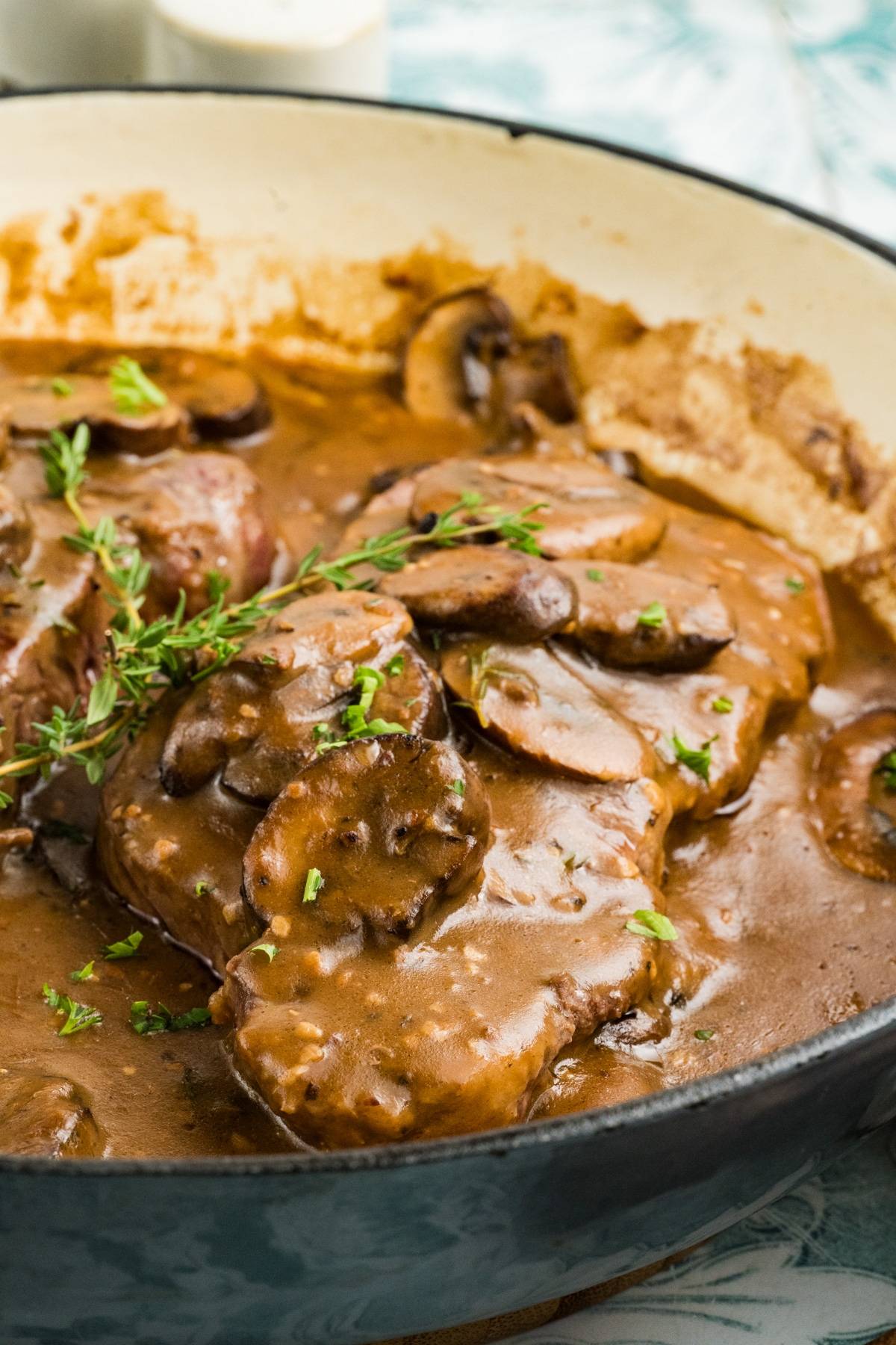 Beef medallions topped with creamy mushroom sauce and herbs in a skillet.
