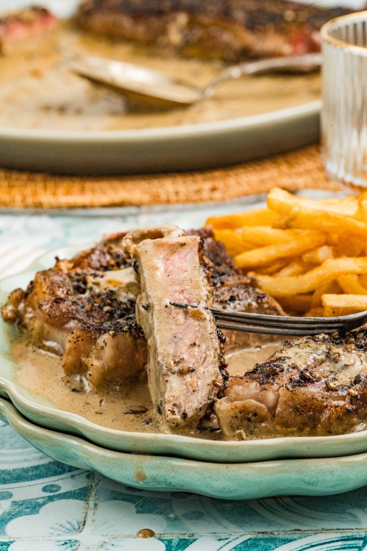 A plate with steak in creamy sauce and a side of French fries, with a fork holding a steak slice.