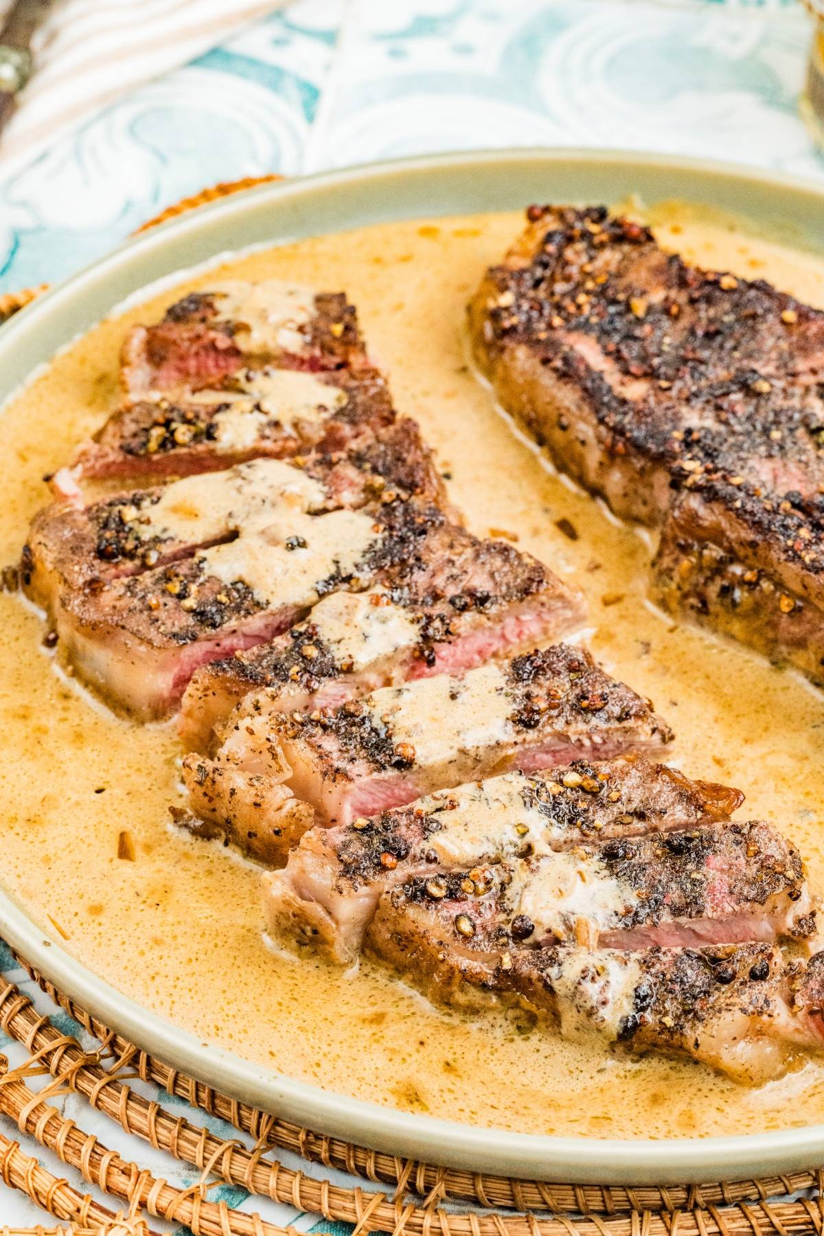 Two grilled steaks in a creamy pepper sauce, one sliced and one whole, served on a beige plate.