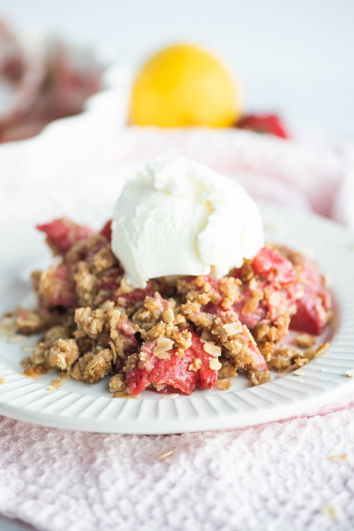 A plate of strawberry crumble or crisp topped with a scoop of vanilla ice cream sits on a pink cloth—a delightful dessert made with fresh berries.