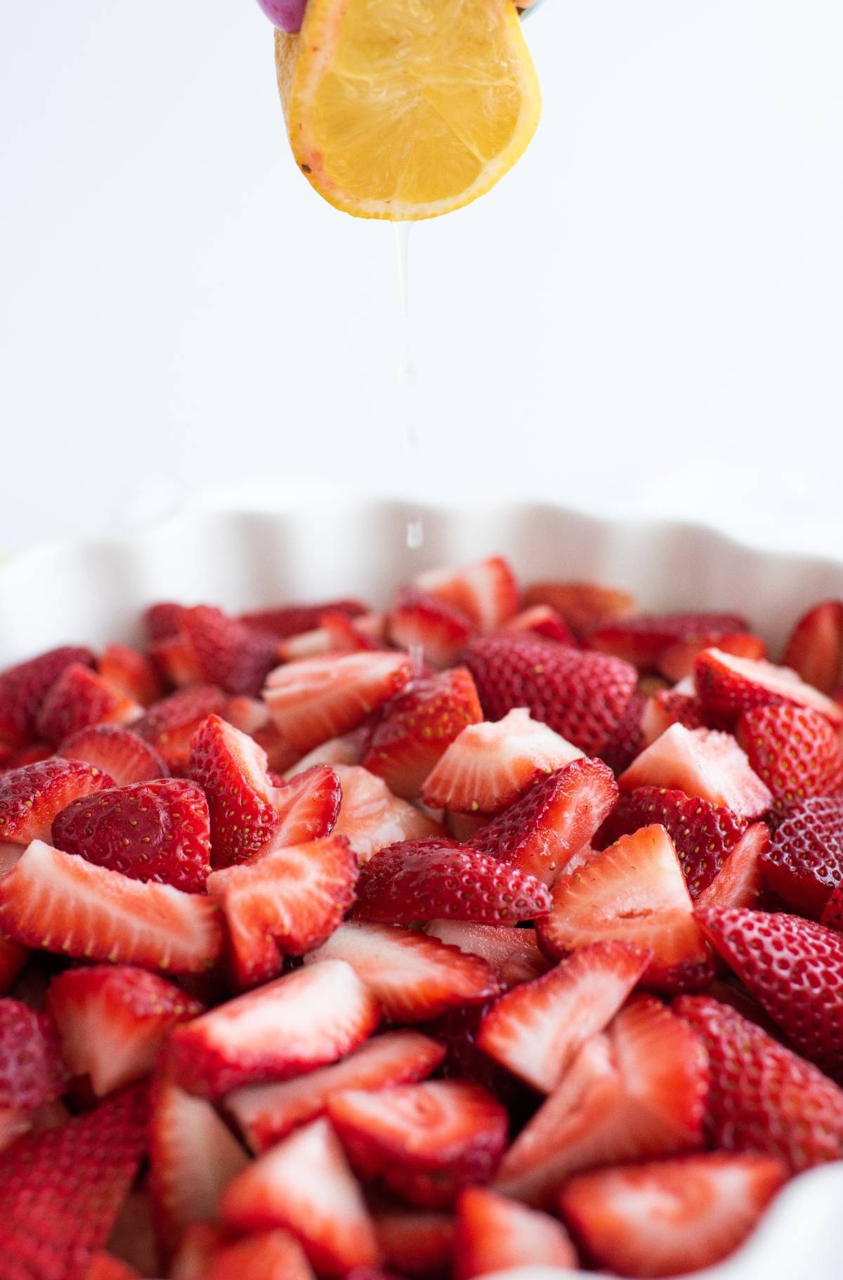 Hand squeezing lemon juice over a dish filled with sliced fresh strawberries, perfect for making a refreshing Strawberry Crisp or baked dessert with fruit.
