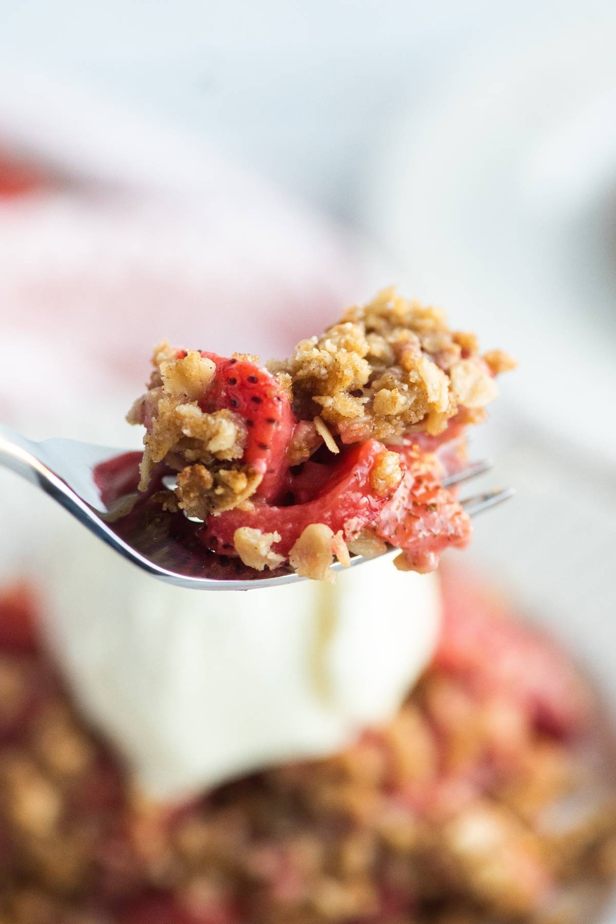 A fork holding a bite of strawberry crumble or crisp with oats, above a scoop of vanilla ice cream—a classic baked dessert with fruit that's perfect for any occasion.