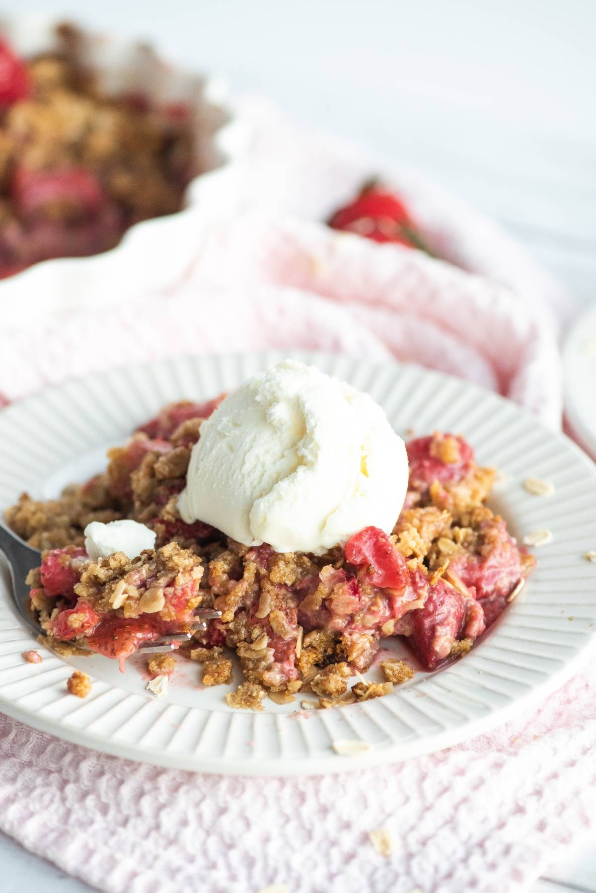 A plate of strawberry crisp topped with a scoop of vanilla ice cream on a white plate, this dessert made with fresh berries is the perfect sweet treat.