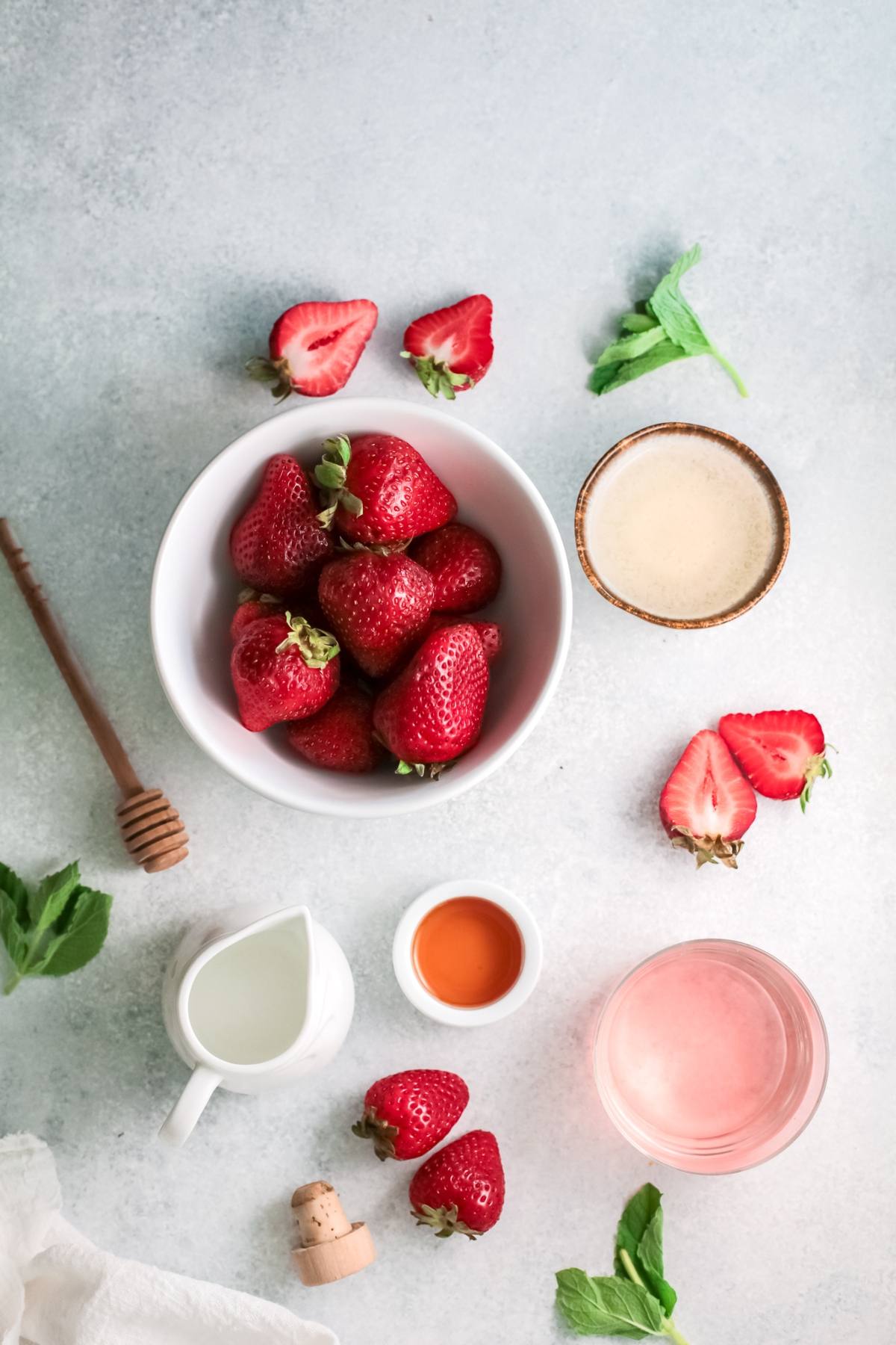 A bowl of strawberries with honey, milk, sauce, mint leaves, and sliced strawberries—perfect for pairing with your favorite strawberry tequila cocktail on a light surface.