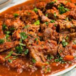 Beef stracotto pot roast in rich tomato sauce garnished with chopped parsley on a white platter.