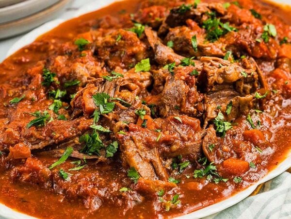 Beef stracotto pot roast in rich tomato sauce garnished with chopped parsley on a white platter.