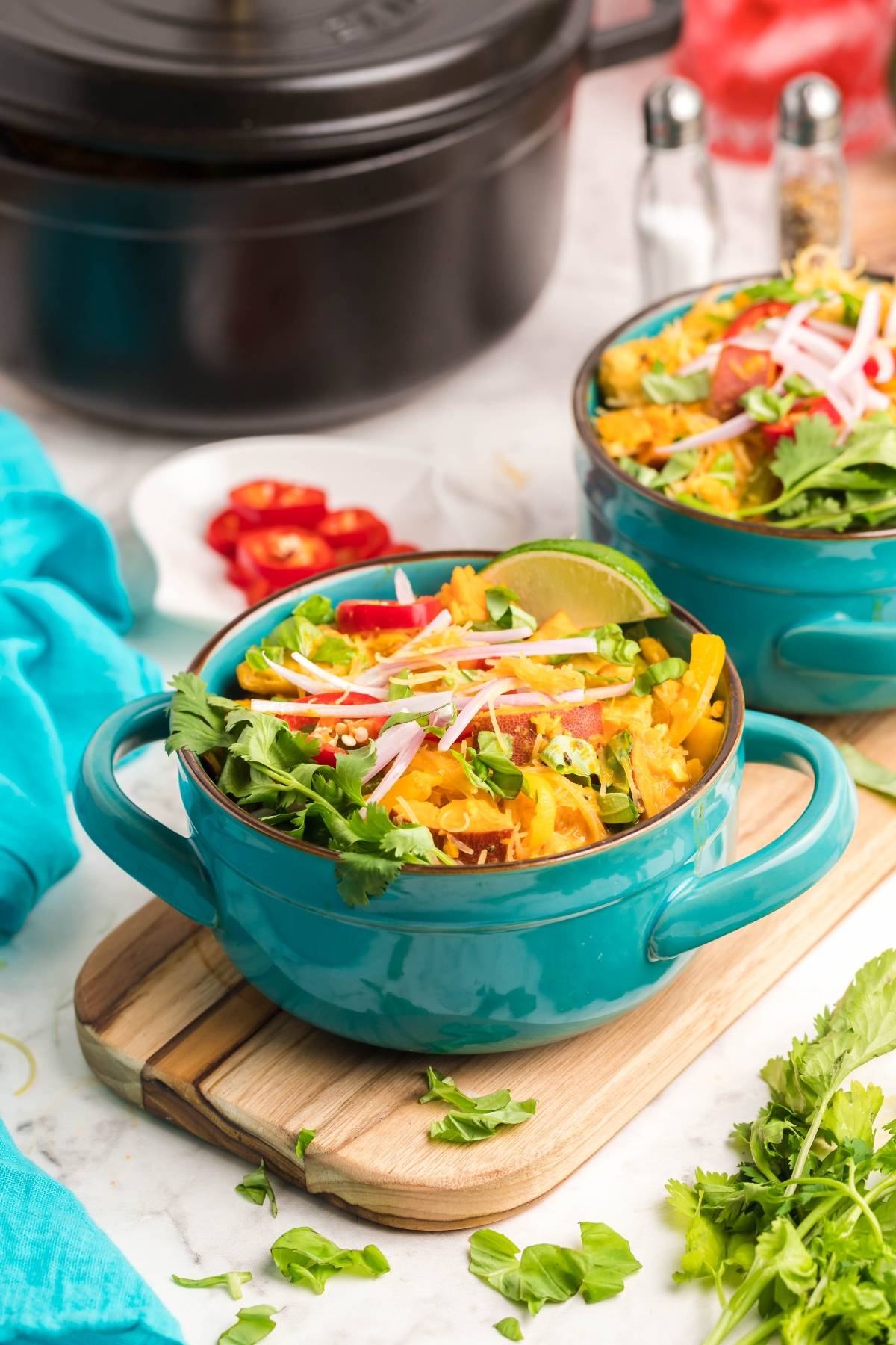 A blue bowl filled with a colorful salad, topped with lime, cilantro, cheese, and sliced radishes—perfect alongside a hearty Thai recipe with chicken.