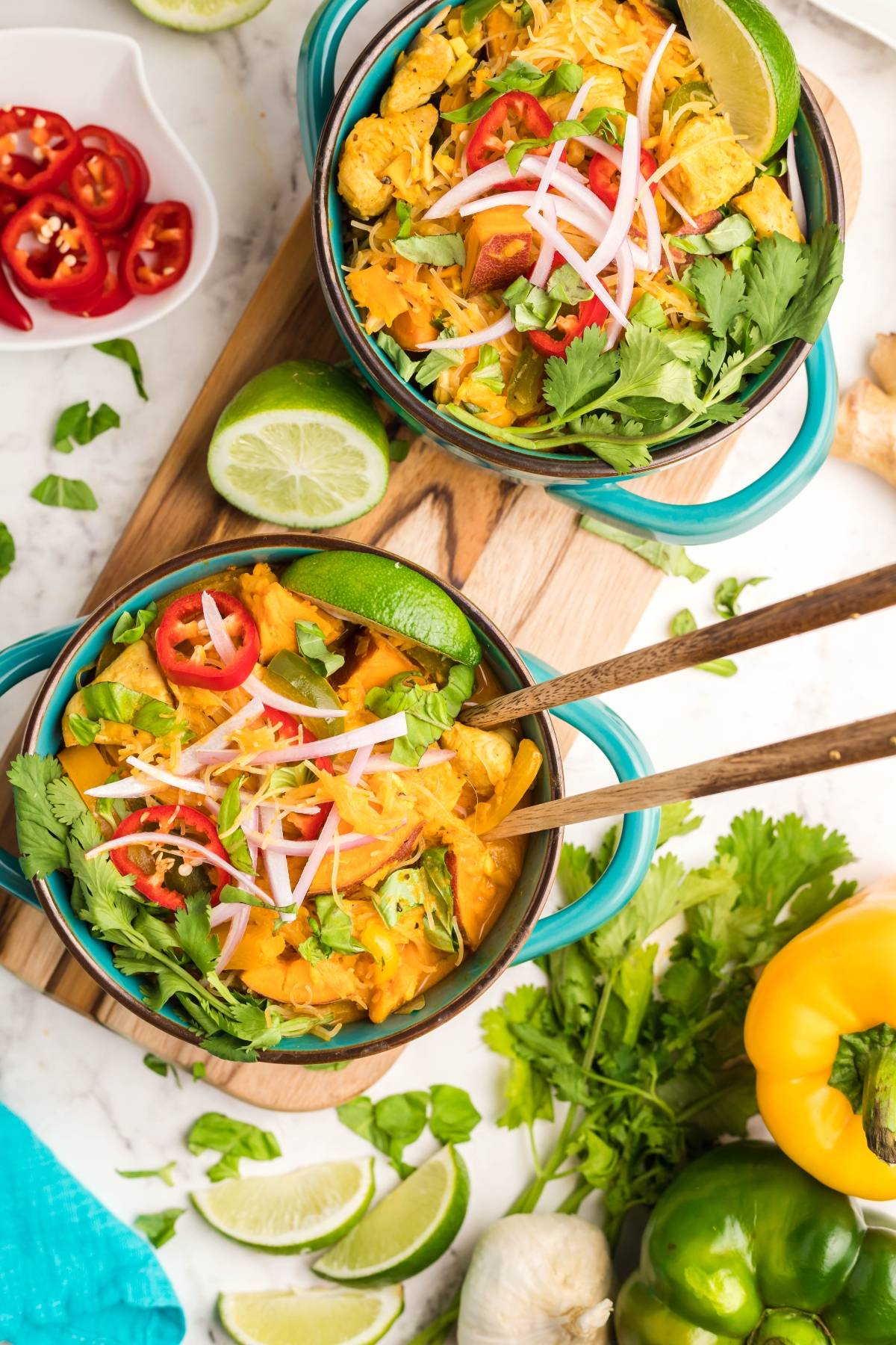 Two bowls of hearty Thai Chicken and Sweet Potato Soup with colorful vegetables, garnished with cilantro, lime, and sliced red chilies.