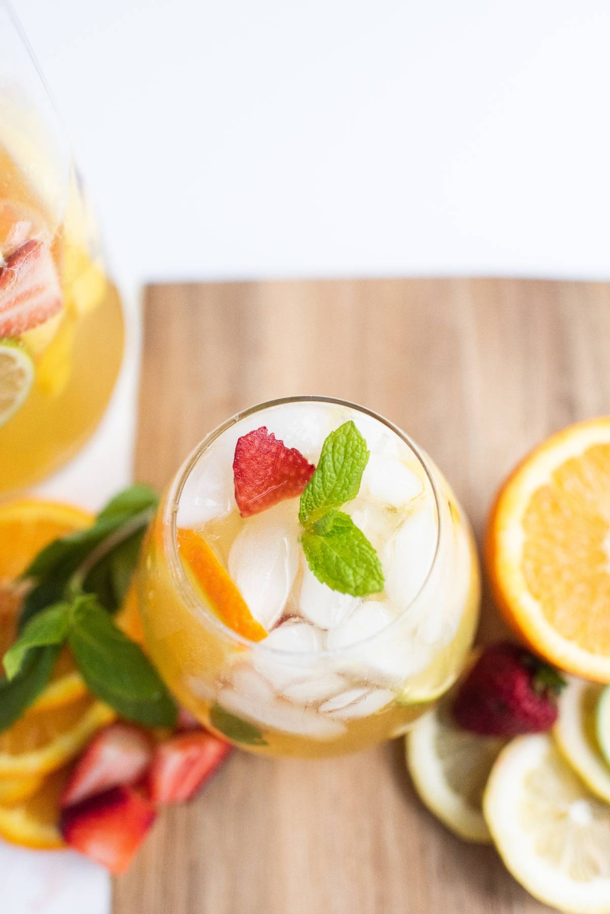 A glass of iced fruit punch with mint, strawberries, and orange slices on a wooden board—this refreshing summer drink is the perfect super easy sangria recipe for any occasion.