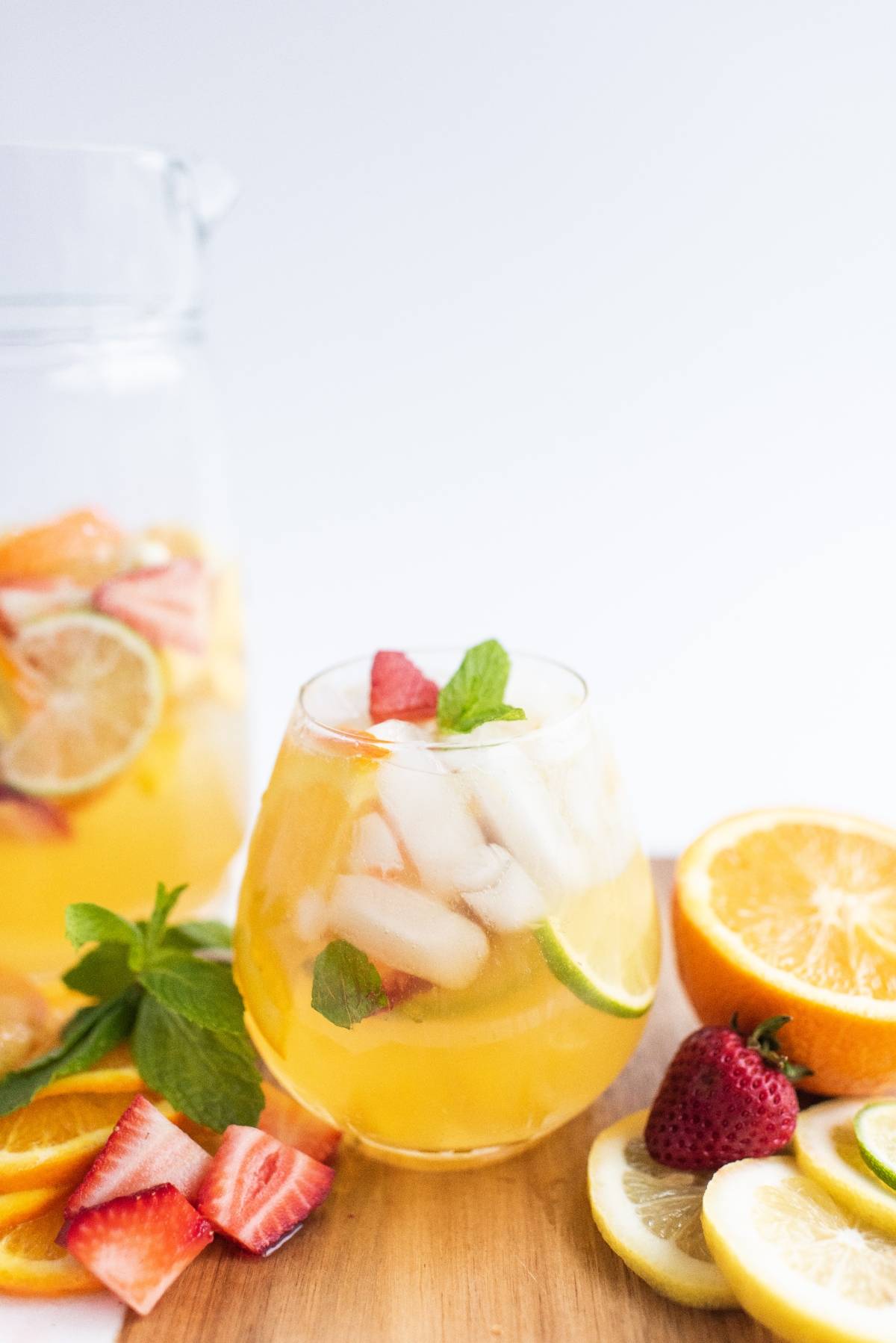 A glass of iced fruit punch with strawberries, lime, orange slices, and mint on a wooden board—perfect inspiration for a refreshing white sangria with summer fruit.