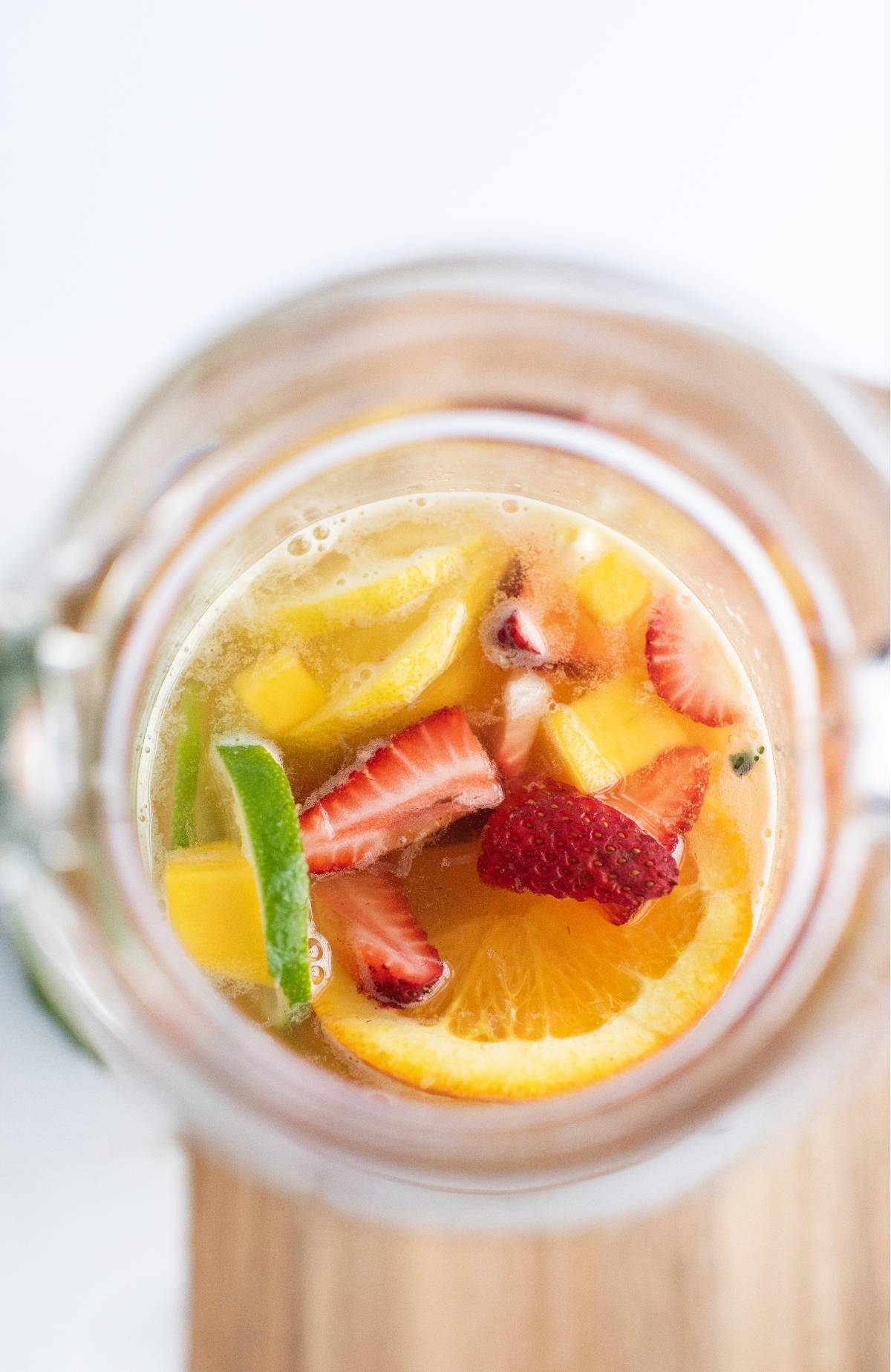 A pitcher filled with slices of orange, lime, strawberries, and other fruits in this super easy sangria recipe for white sangria with summer fruit.