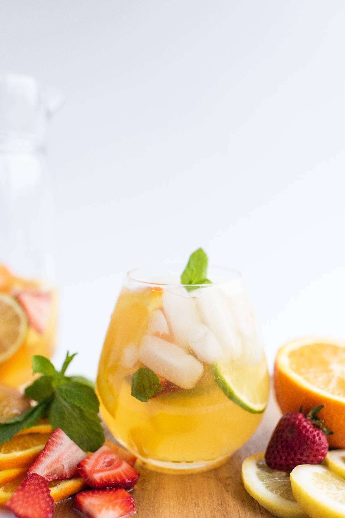 A glass of iced fruit punch with mint, surrounded by fresh strawberries, lemon, orange, and lime slices—a refreshing summer drink reminiscent of a super easy sangria recipe.