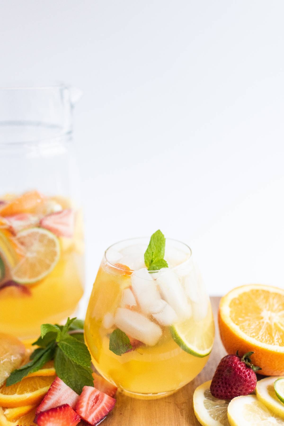 A glass of iced citrus and strawberry punch with mint, surrounded by fresh fruit slices on a wooden board—perfect for a white sangria with summer fruit and an irresistibly refreshing, super easy sangria recipe.